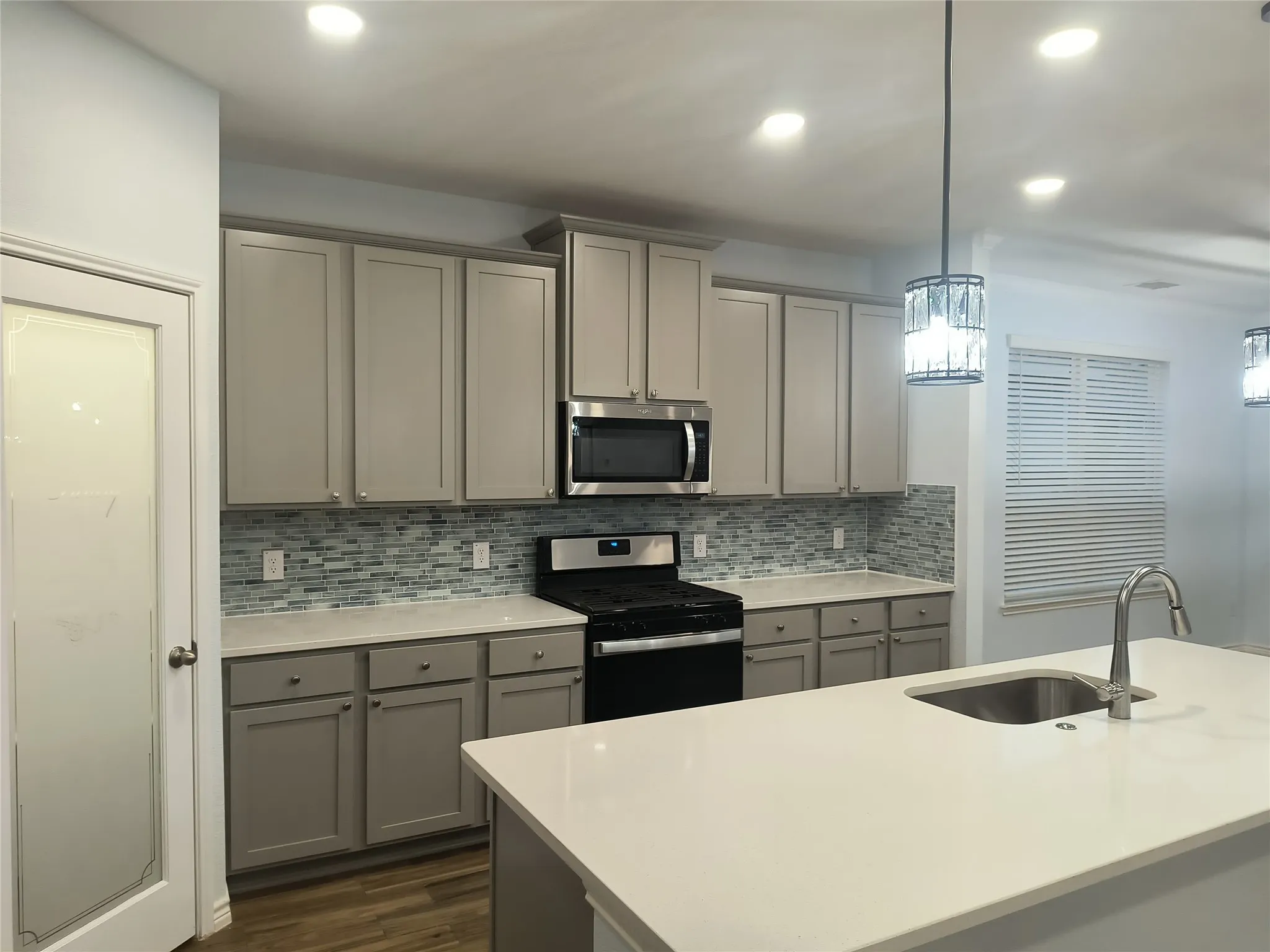 Contemporary kitchen featuring light gray cabinetry, a mosaic tile backsplash, and light-toned countertops