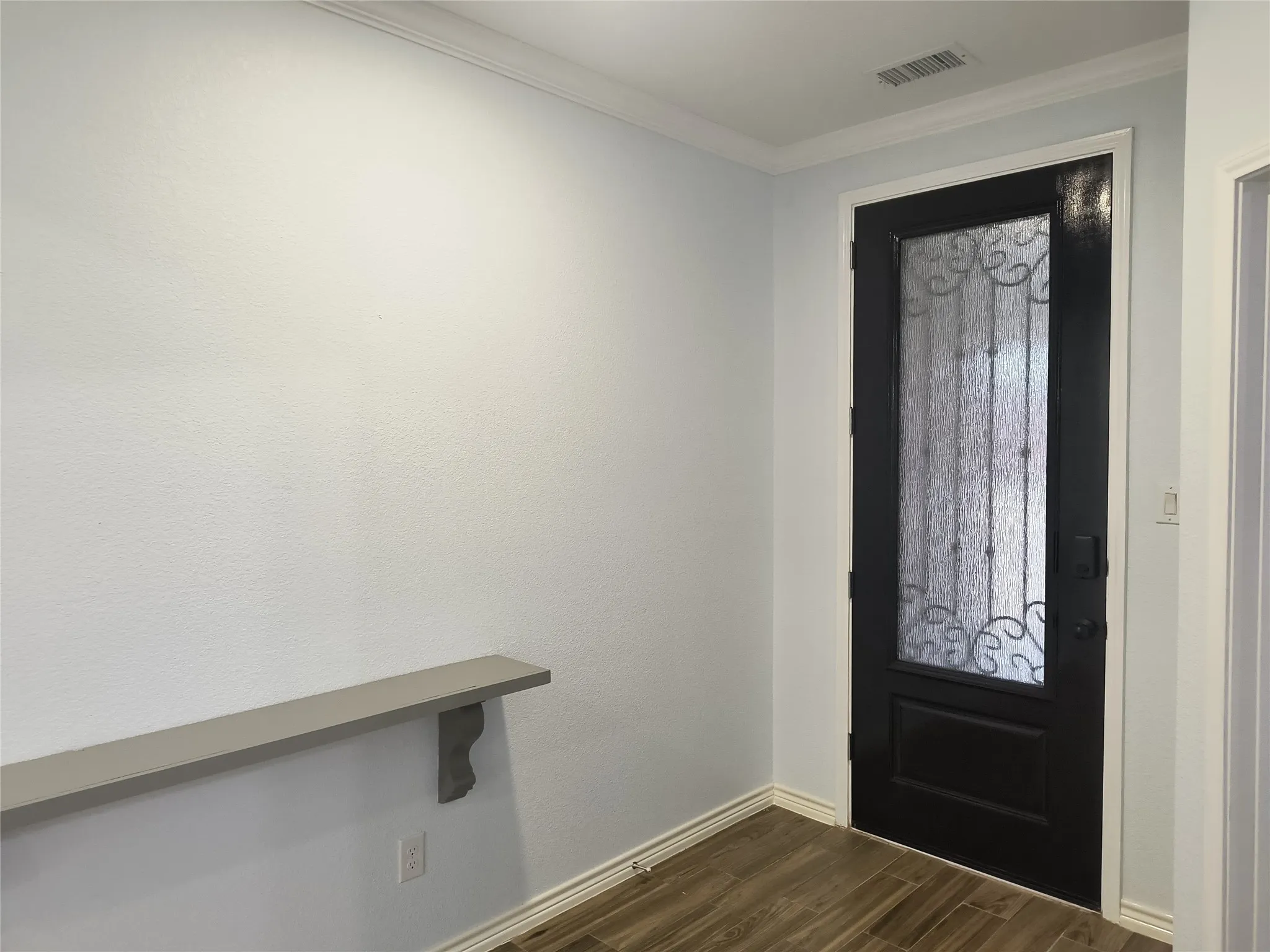 Black entry door with frosted glass and decorative ironwork, complemented by light wood-finish flooring