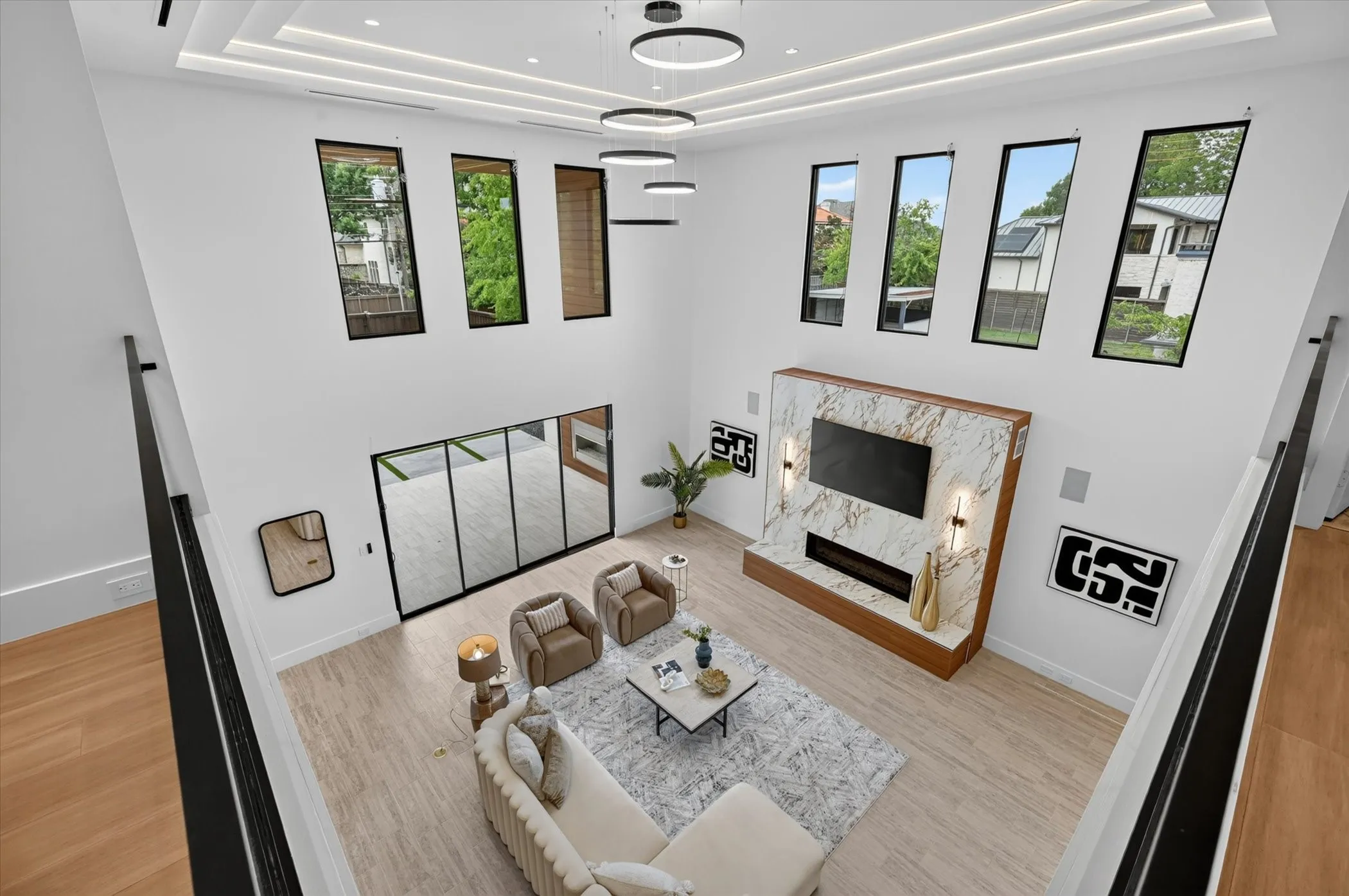 Two-story living area with high ceilings, featuring a fireplace with a stone surround, multiple transom windows, wood-finish flooring, and a contemporary ceiling light fixture