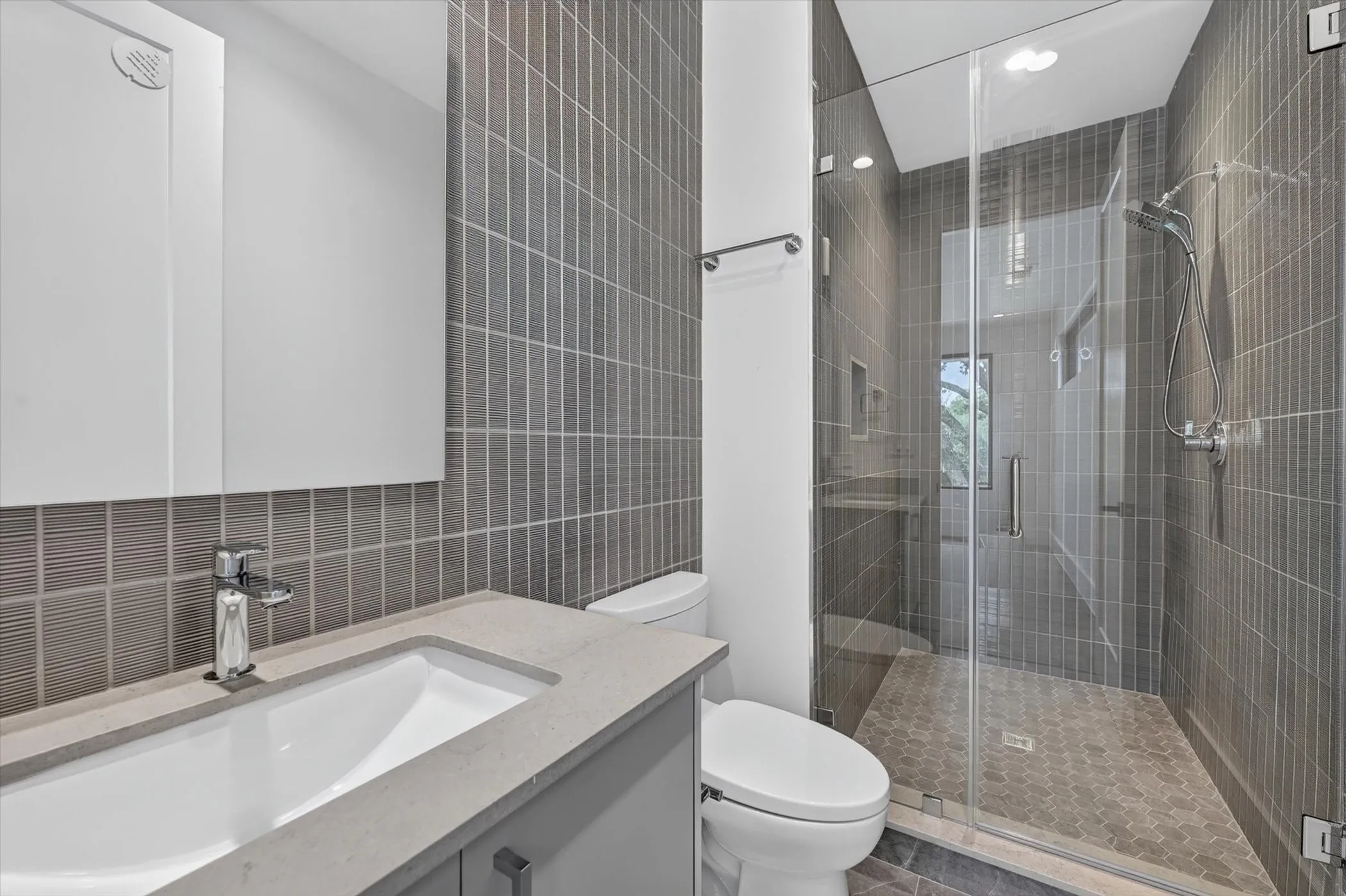 Modern bathroom featuring a walk-in shower with clear glass enclosure, gray vertical subway tile, and hexagon floor tile