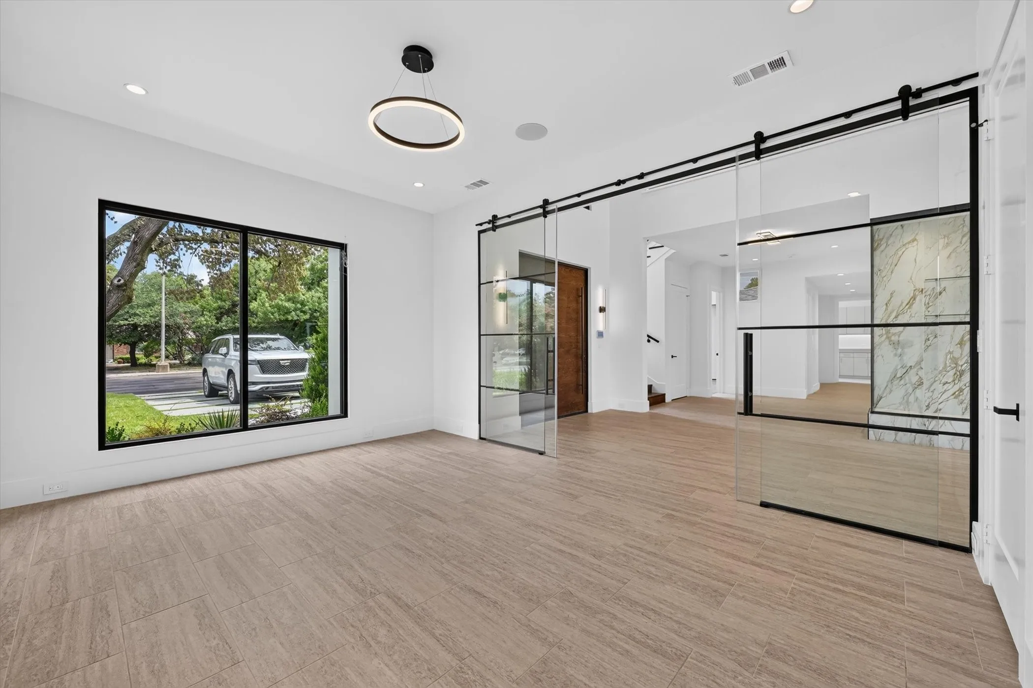 Contemporary interior featuring wood-finish flooring, a large window with black trim, and a modern circular pendant light