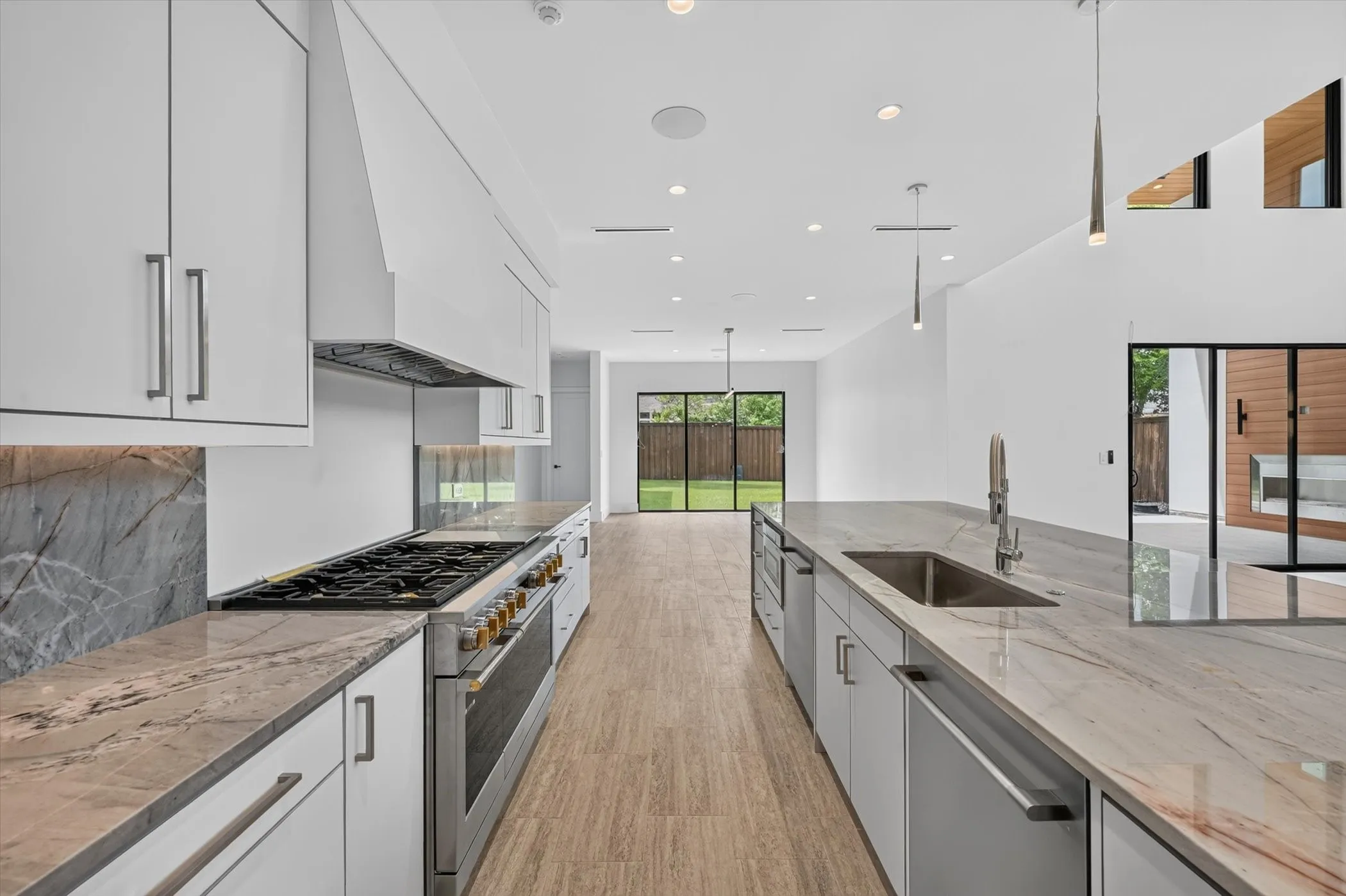 Contemporary kitchen featuring light wood-finish flooring, white cabinetry, integrated stainless steel appliances, and stone countertops