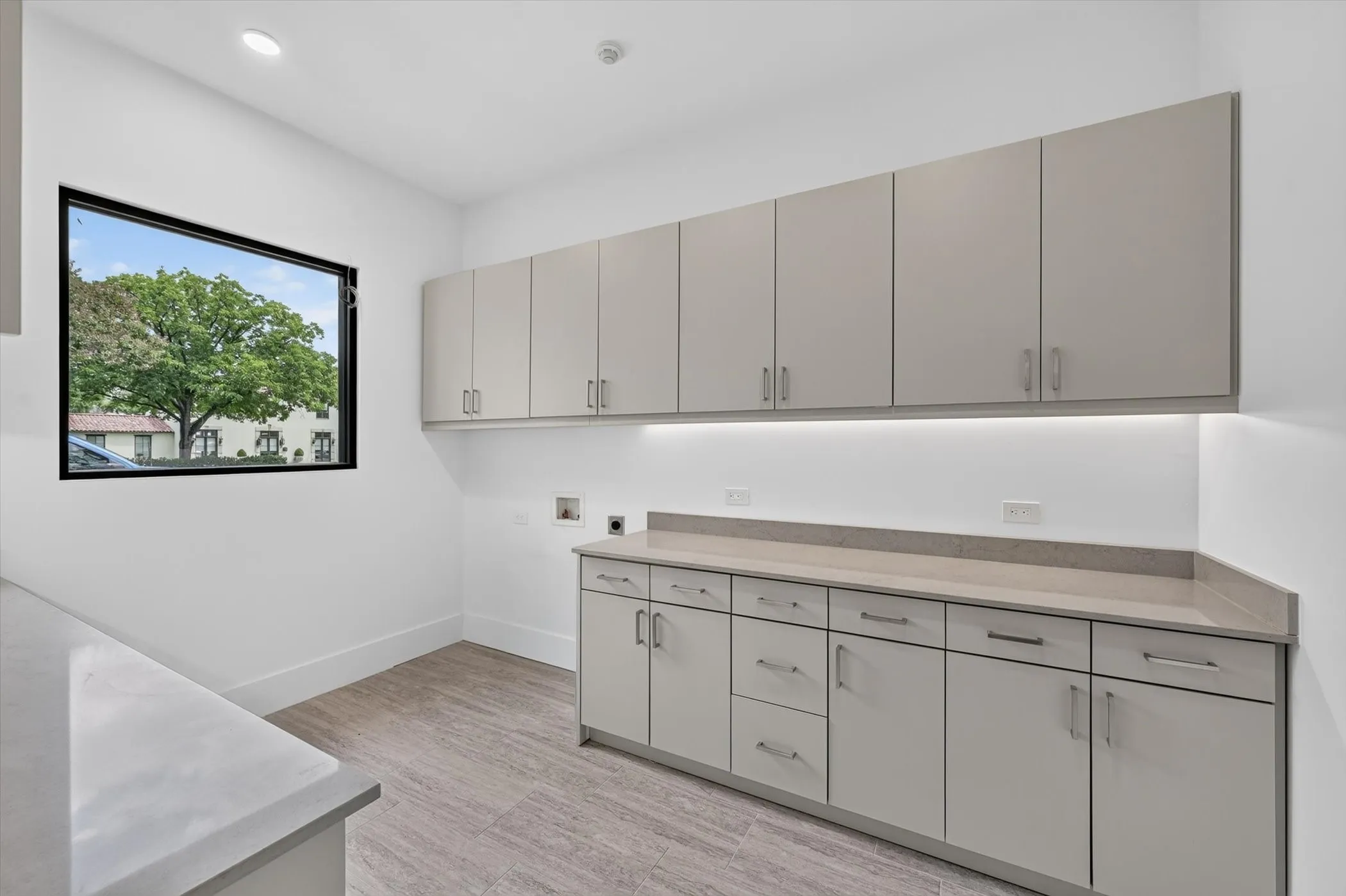 Spacious utility room featuring extensive built-in cabinetry, stone-finish countertops, under-cabinet lighting, and wood-finish flooring