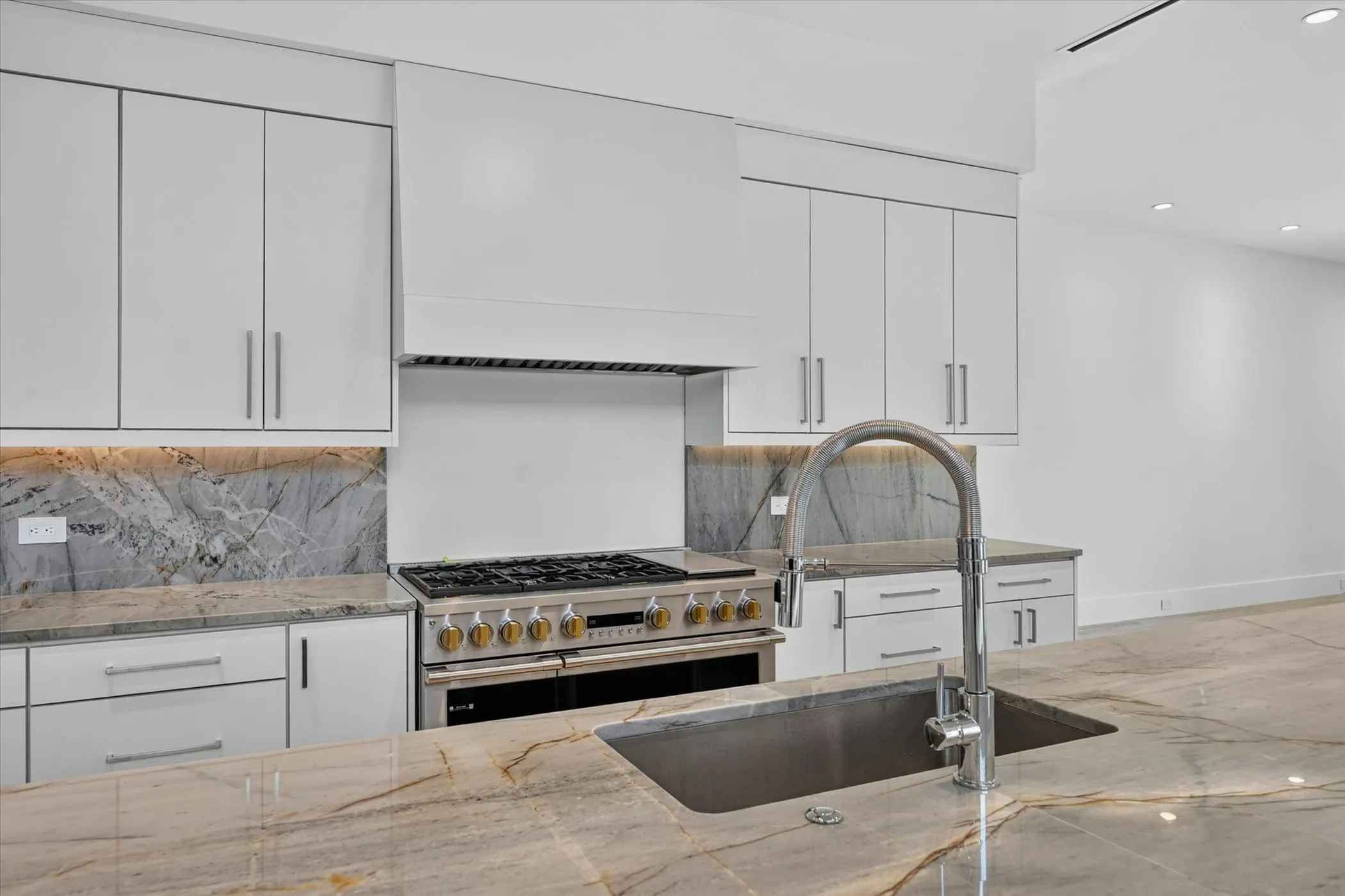 White cabinetry with under-cabinet lighting, full-height stone backsplash, stainless steel range with ventilation hood, and a large kitchen island with an undermount sink and gooseneck faucet