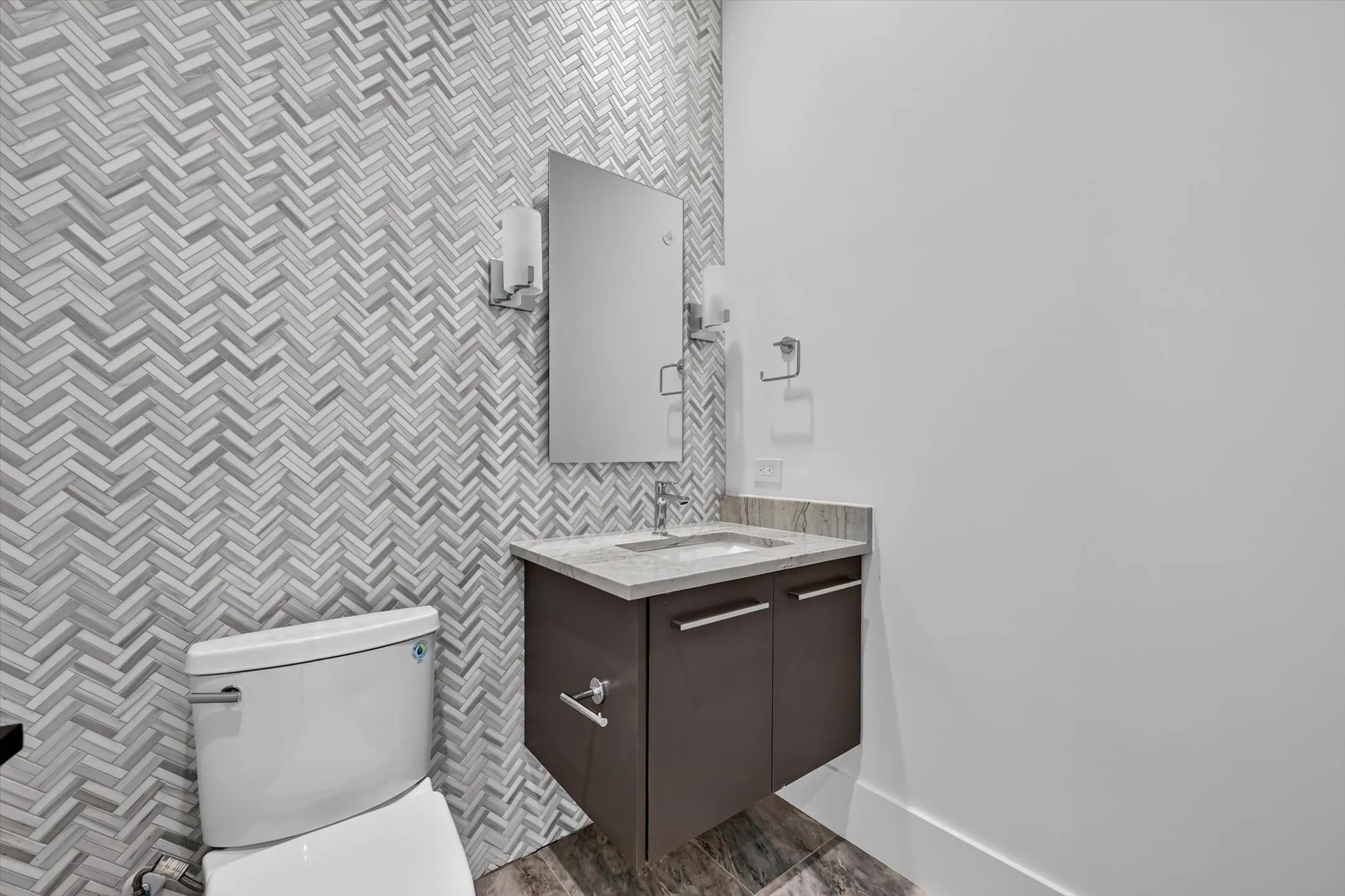 Powder room featuring a herringbone tile accent wall, a wall-mounted vanity with a light-toned countertop, a rectangular mirror, and chrome fixtures