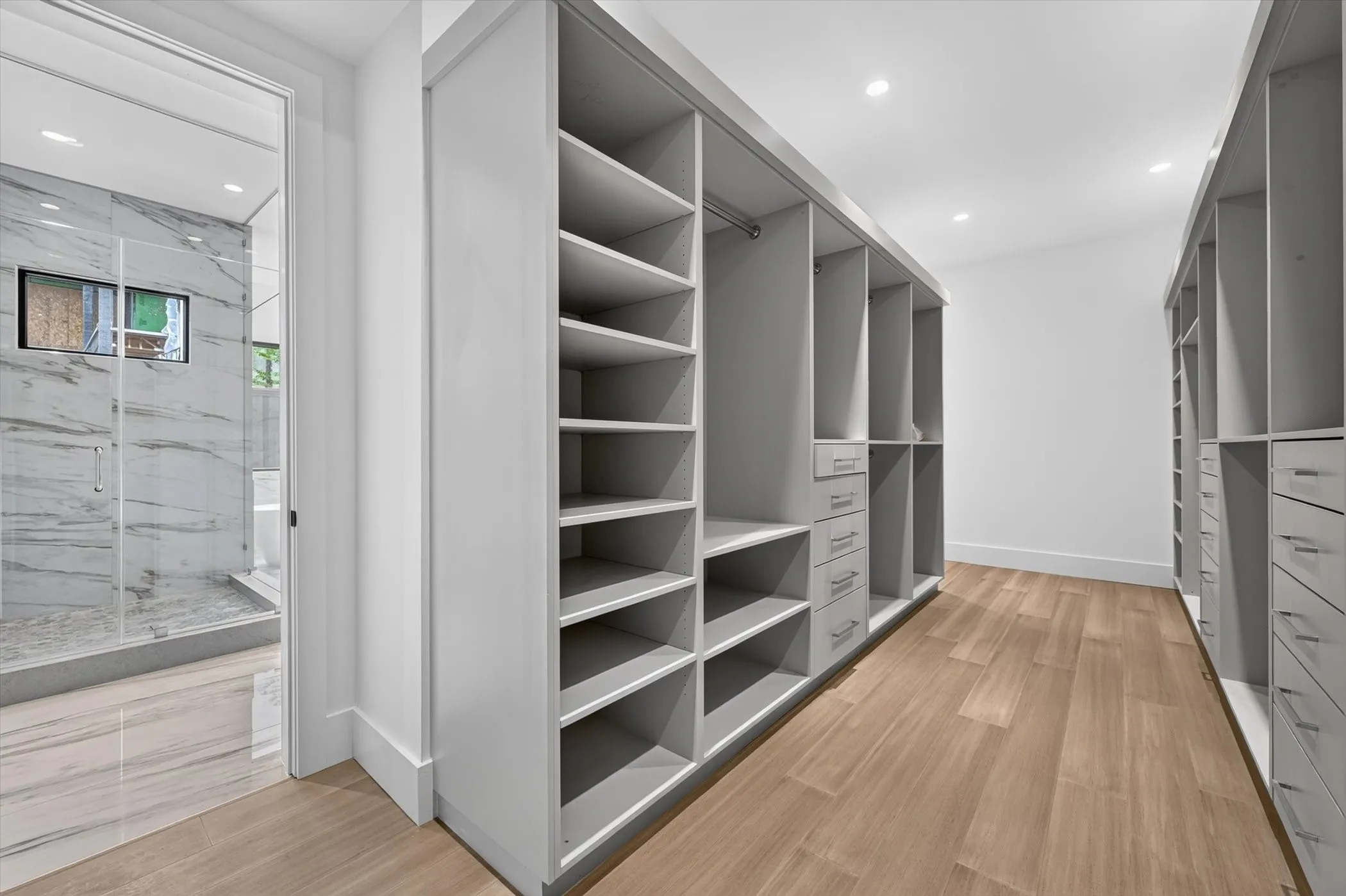 Luxurious walk-in closet featuring extensive built-in shelving and cabinetry with multiple compartments, warm wood-finish flooring, recessed lighting, and a spacious layout with organized storage solutions throughout