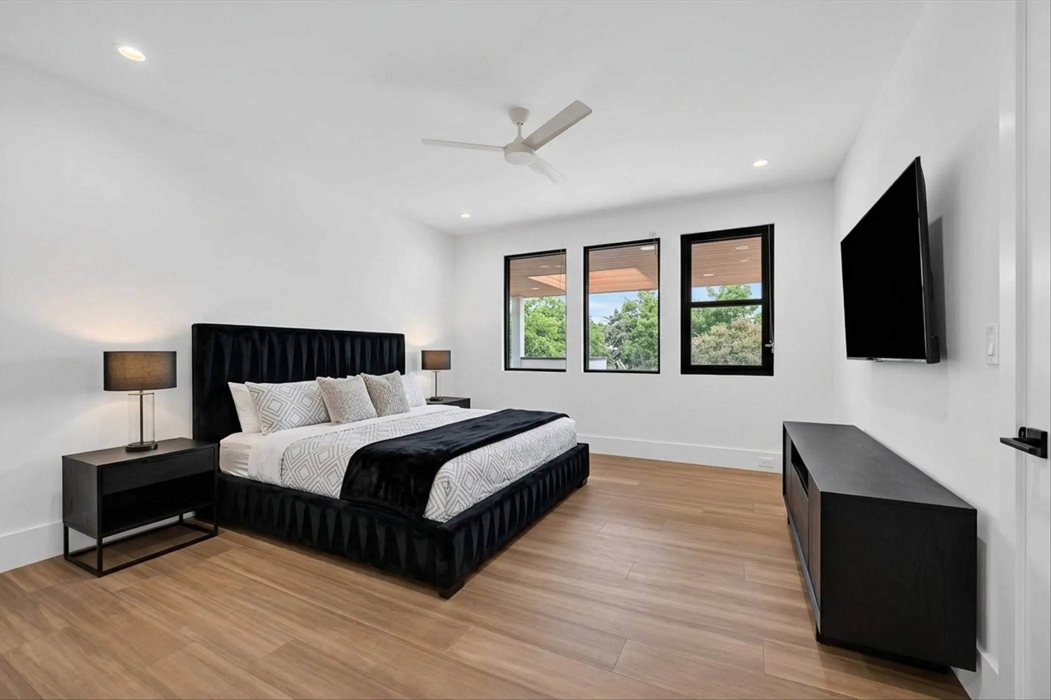 Recessed lighting, wood-finish flooring, white walls, black-framed windows, and a ceiling fan