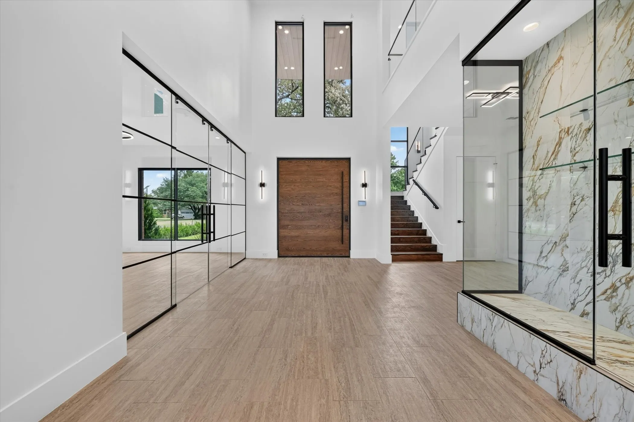 Two-story entryway featuring a solid wood door, wood-finish flooring, and a contemporary glass wall partition