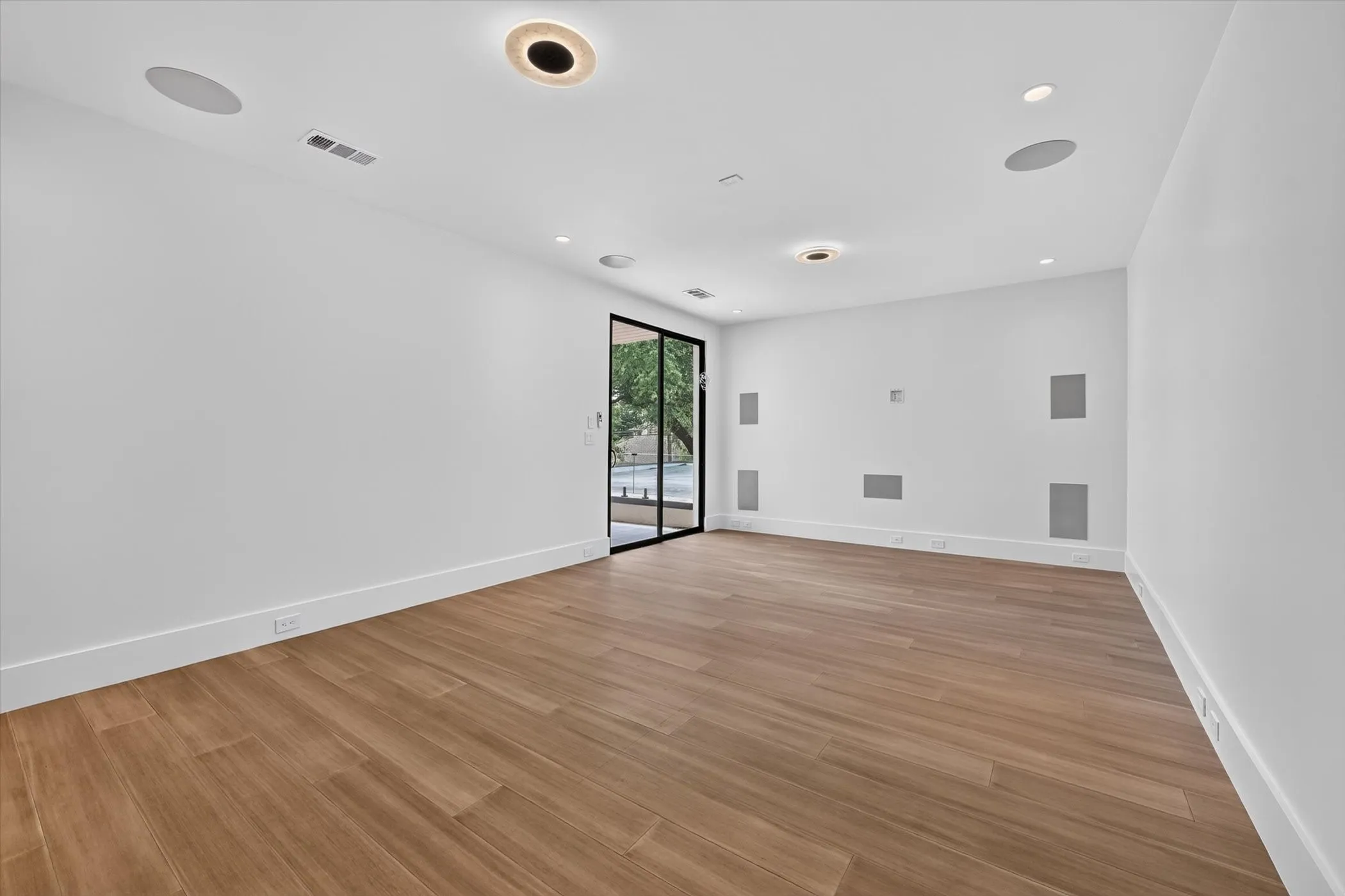 Spacious room featuring wood-finish flooring, recessed lighting, and integrated wall speakers