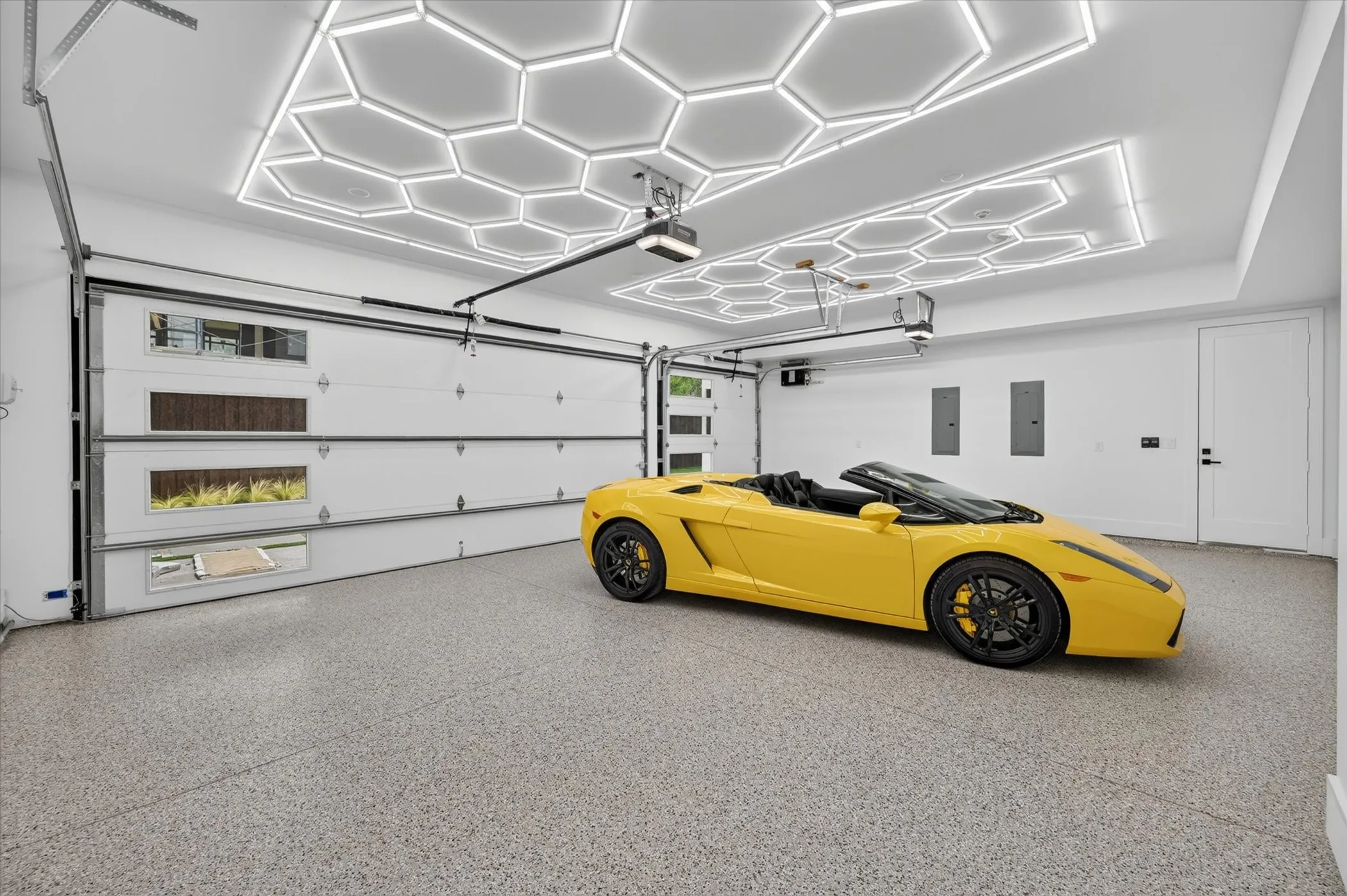Spacious garage featuring a durable epoxy floor finish, custom hexagonal ceiling lighting, and overhead garage door with integrated windows