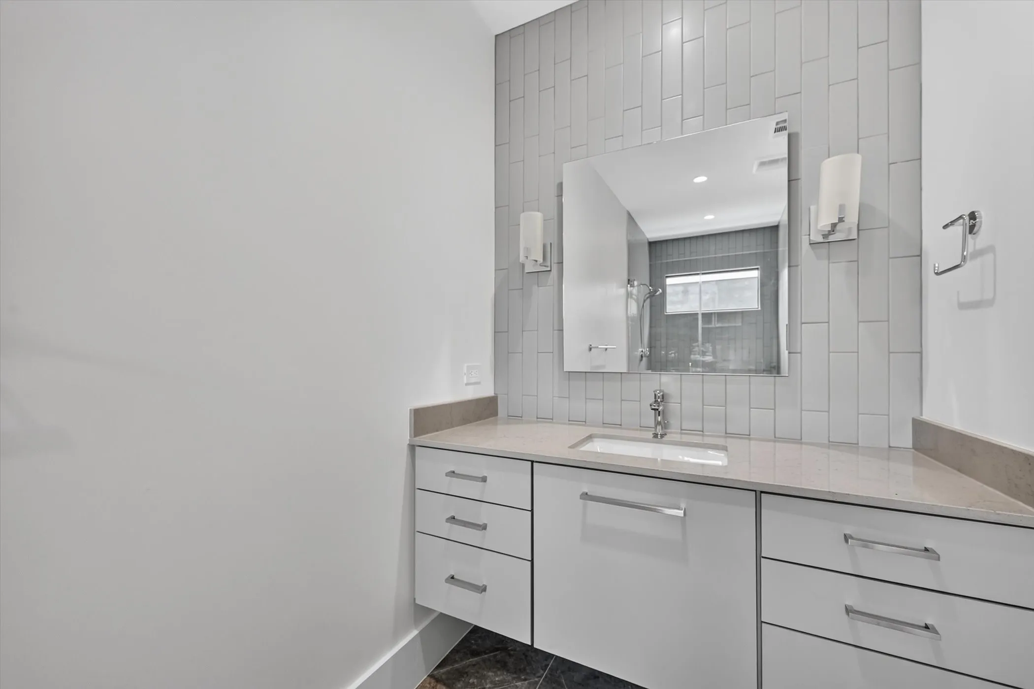 Contemporary vanity featuring white cabinetry with polished chrome hardware, an integrated sink, and a light-toned countertop