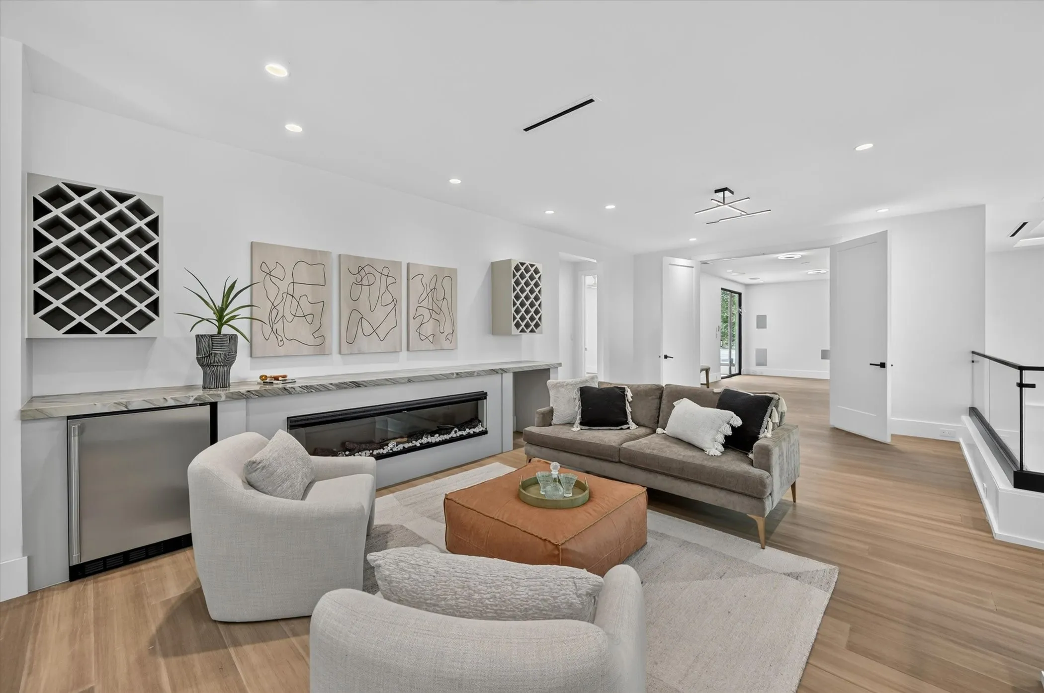Integrated linear fireplace with a stone surround, built-in wine storage, wood-finish flooring, recessed lighting, and a glass and metal railing
