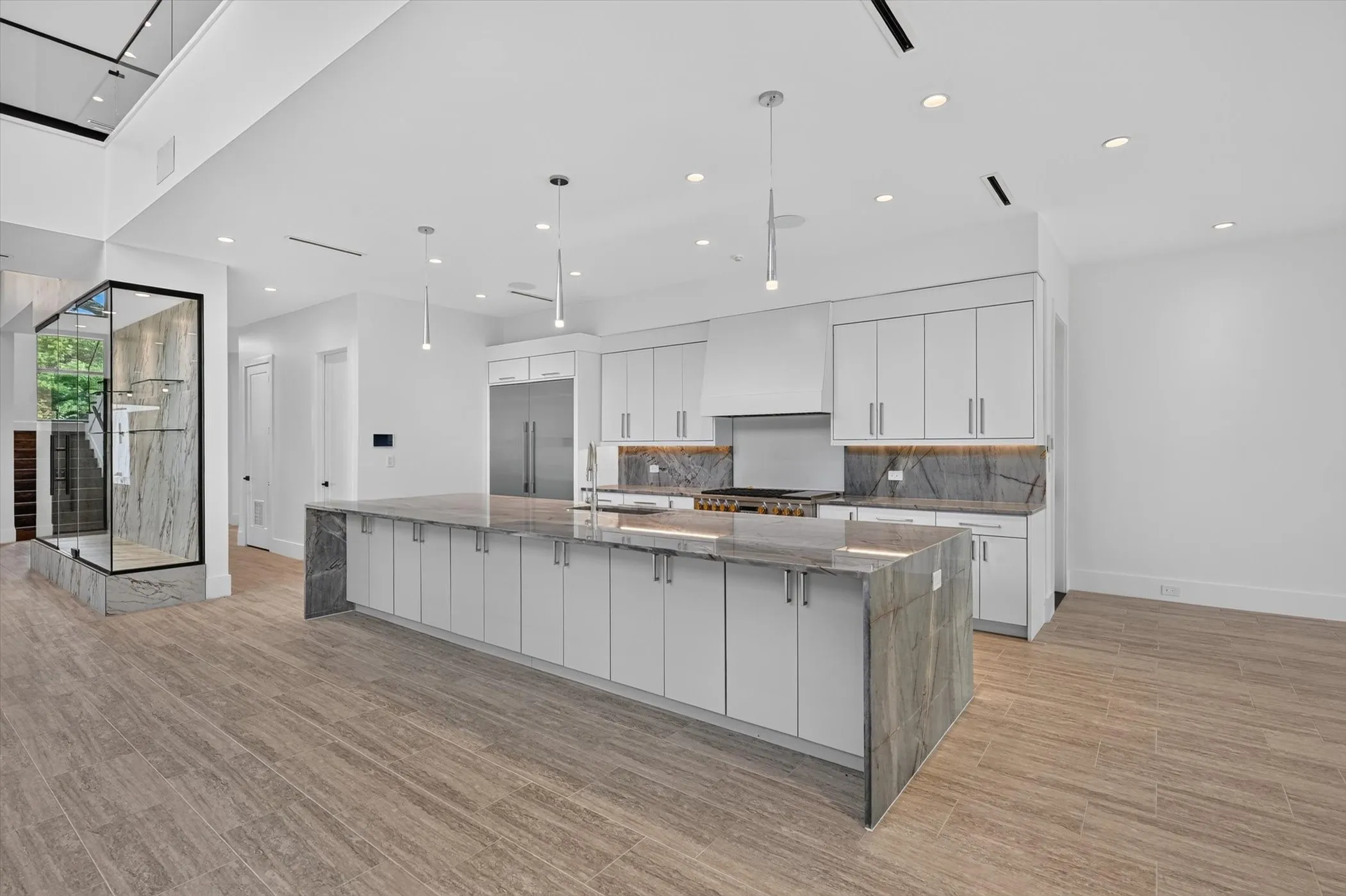 Expansive kitchen featuring a waterfall island with stone countertop, integrated stainless steel appliances, contemporary pendant lighting, and recessed ceiling lights