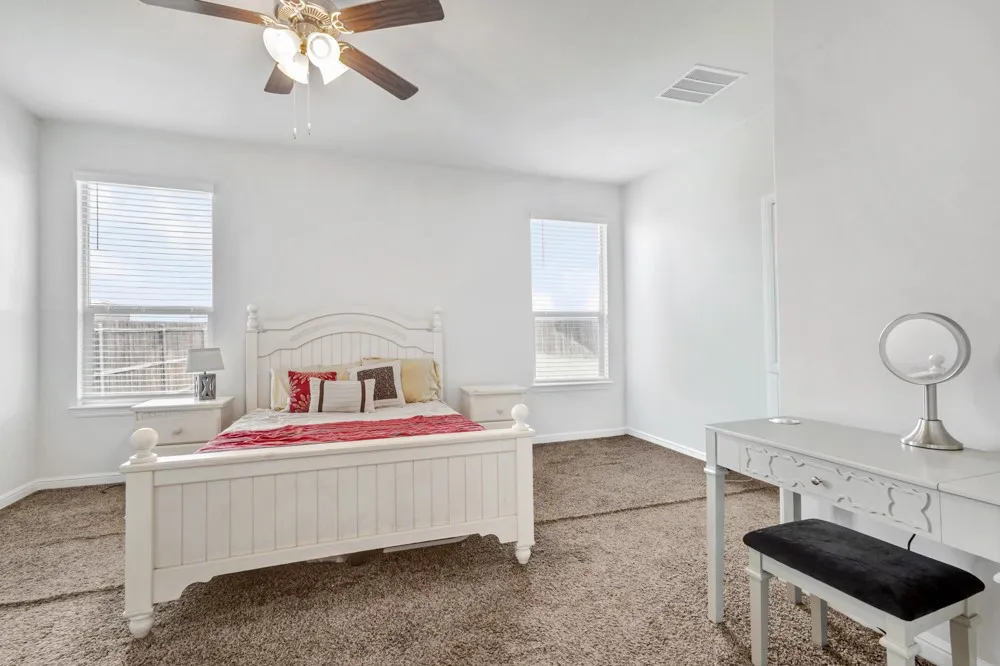 Bright room featuring two windows with blinds, a ceiling fan with light fixture, and carpeted flooring