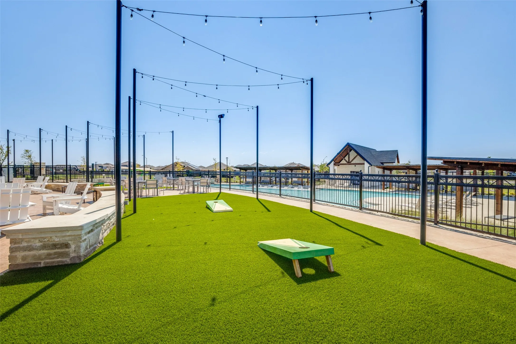 Expansive turf recreation area featuring string lighting and a stone-capped retaining wall