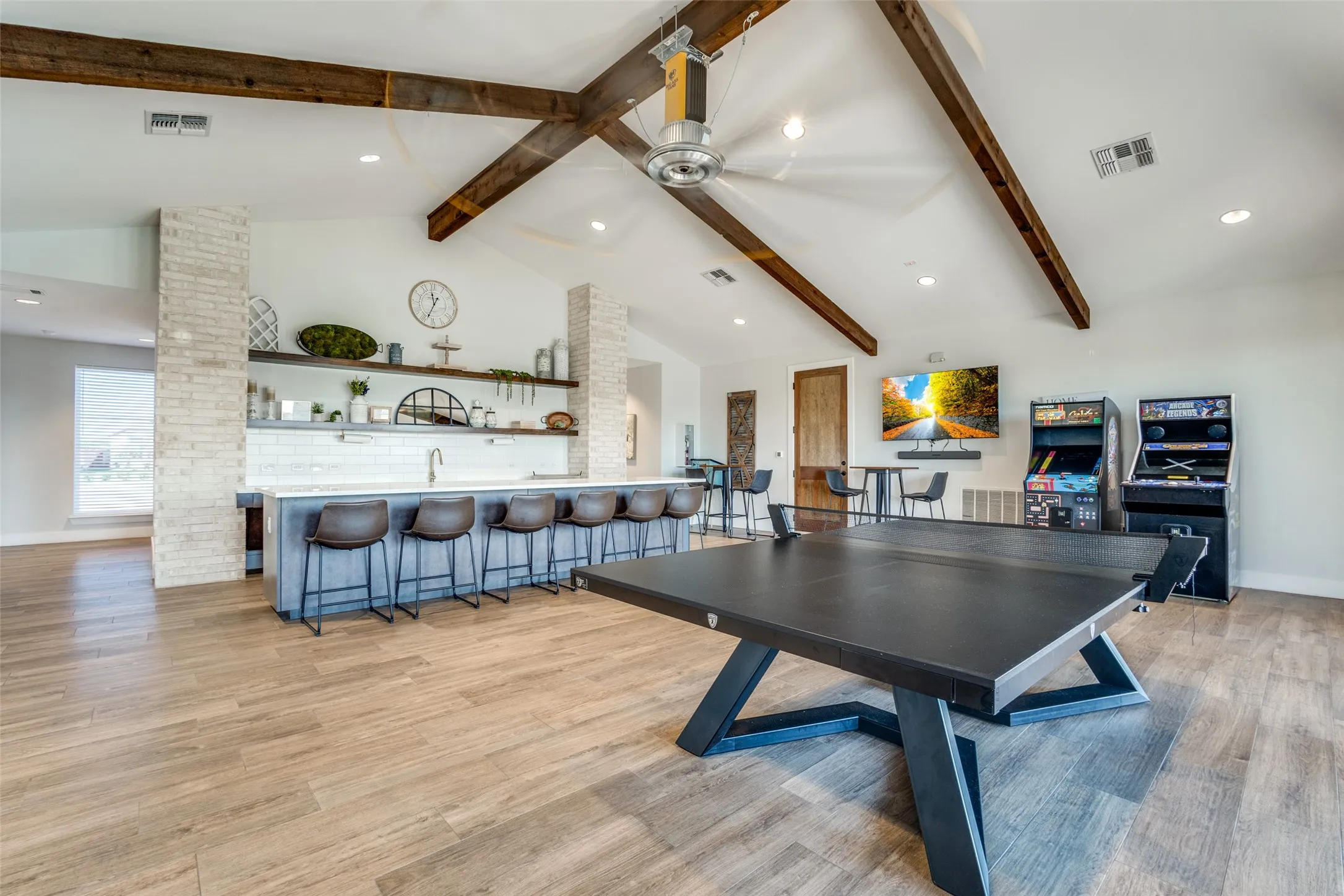 Spacious vaulted ceiling room featuring exposed wood beams and wood-finish flooring