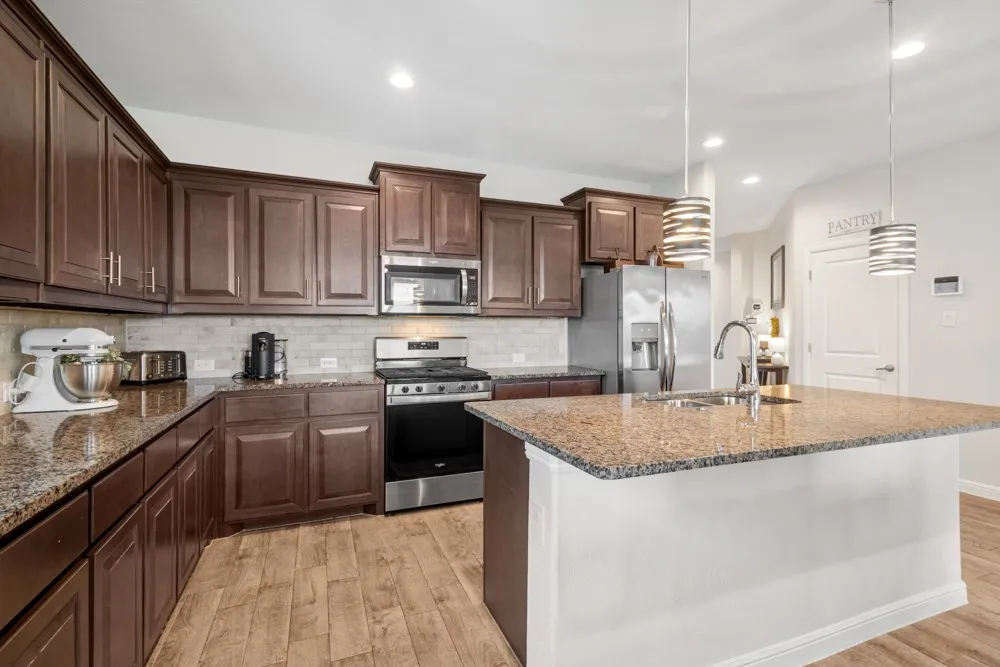 Kitchen featuring an expansive island with a stainless steel sink, granite countertops, wood-finish flooring, dark wood cabinetry, and stainless steel appliances