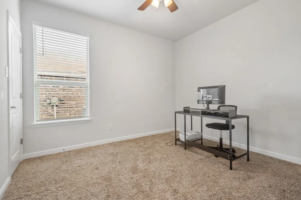 Spacious room with plush carpeting, neutral wall tones, a large window with blinds, and an overhead ceiling fan
