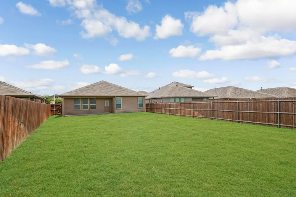 Expansive backyard featuring a lush green lawn, full privacy fencing, and a single-story residence with multiple windows