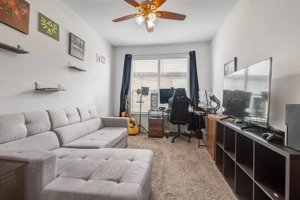 Carpeted room featuring a ceiling fan with light fixture, window with horizontal blinds, and a built-in shelving unit