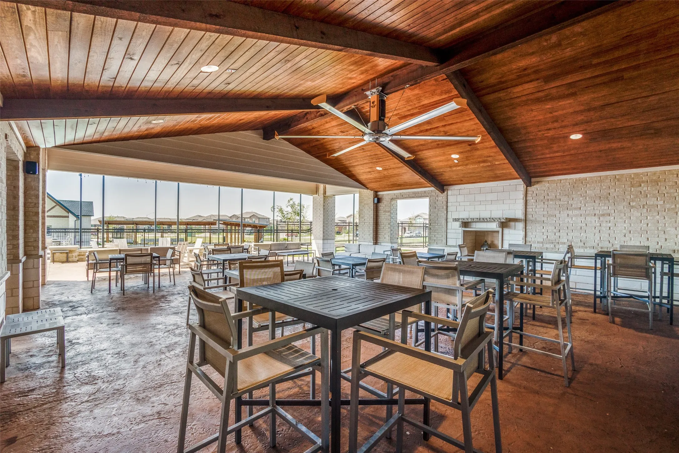 Covered outdoor lounge area featuring a vaulted wood-paneled ceiling, large ceiling fan, and a built-in stone fireplace