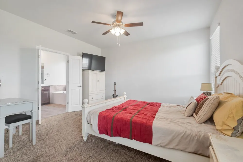 Carpeted bedroom featuring a ceiling fan, window with blinds, and an attached bathroom with a built-in tub