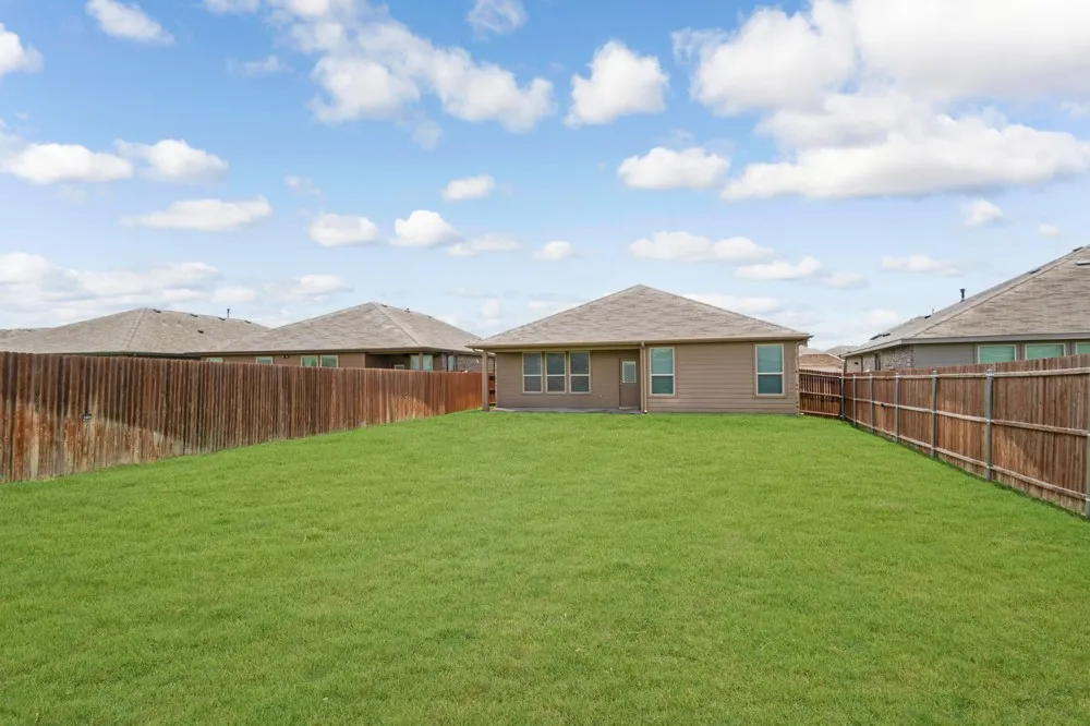 Expansive backyard with a lush green lawn, full privacy fencing, and a single-story residence featuring light brown siding and multiple windows