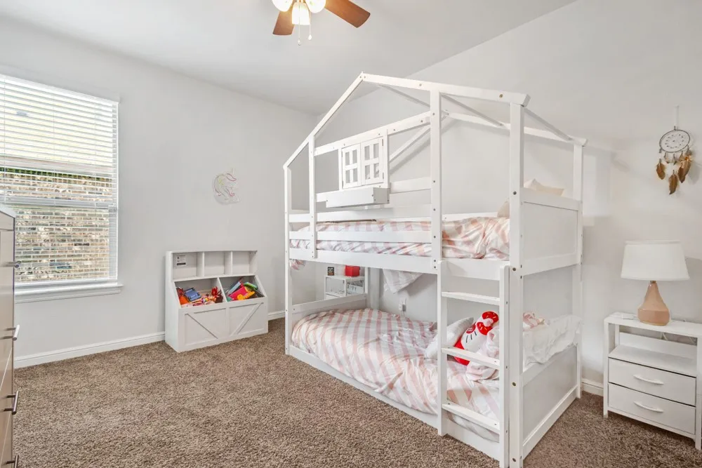 Spacious room with plush carpeting, natural light from a window with blinds, and a built-in ceiling fan with lighting
