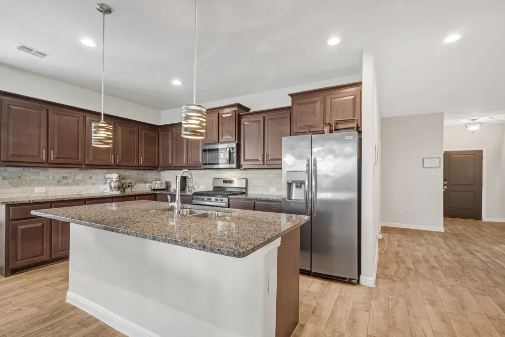 Kitchen featuring a central island with a sink, granite countertops, and dark wood cabinetry