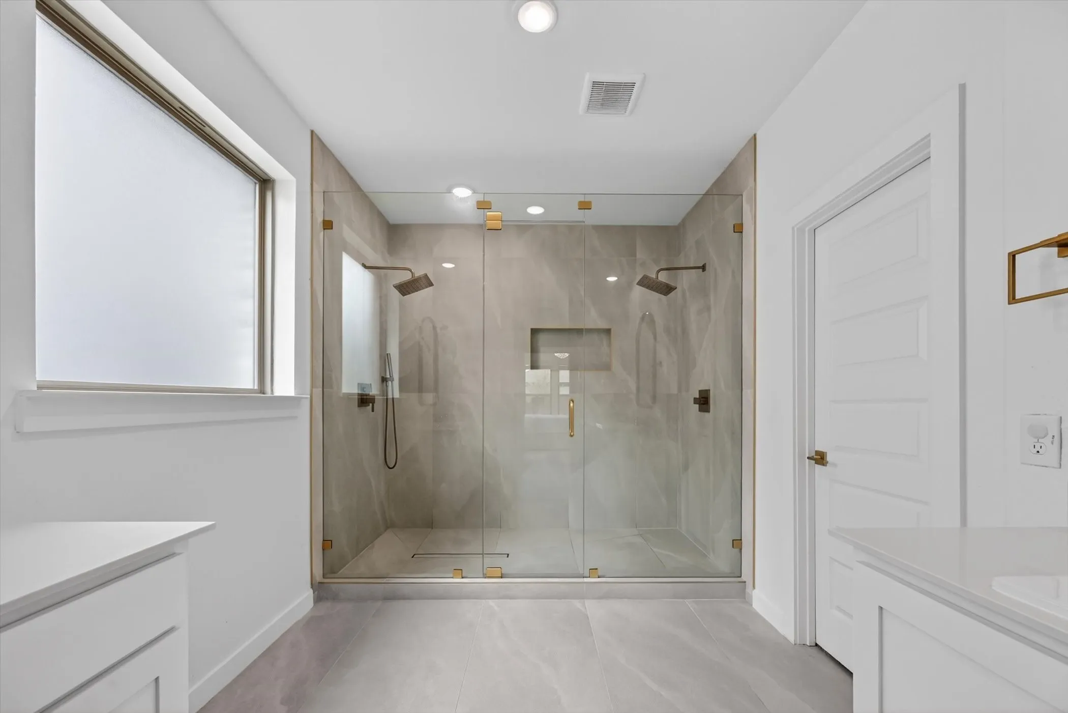 Spacious walk-in shower with clear glass enclosure and dual brass-finish rain showerheads