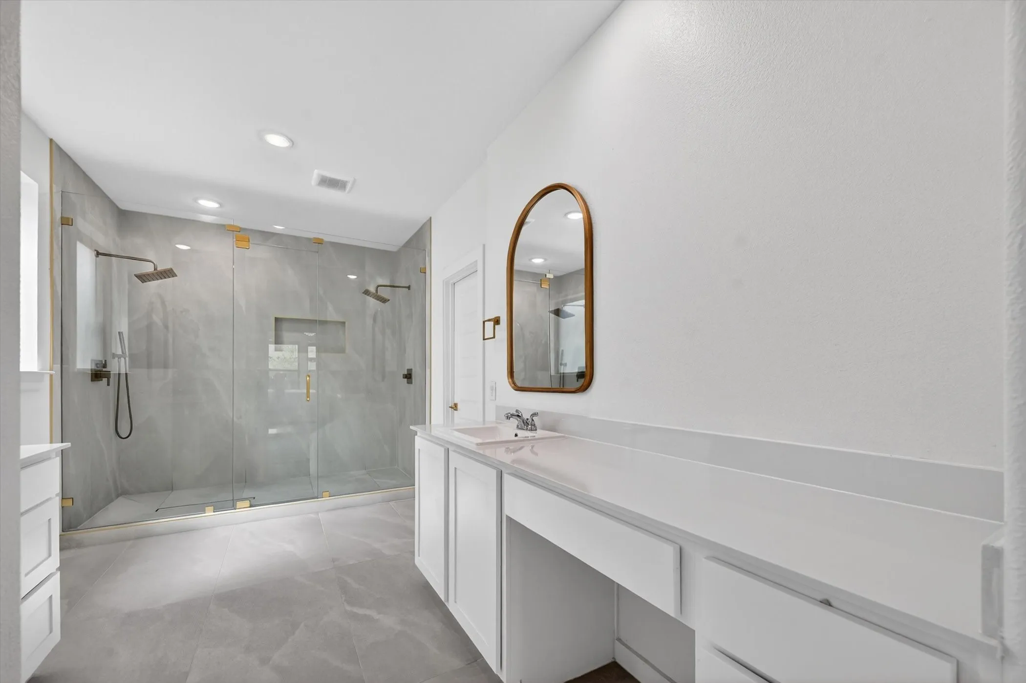 Spacious bathroom featuring a large glass-enclosed shower with dual showerheads and marble-finish tile, white vanity cabinetry, and a countertop with integrated sink