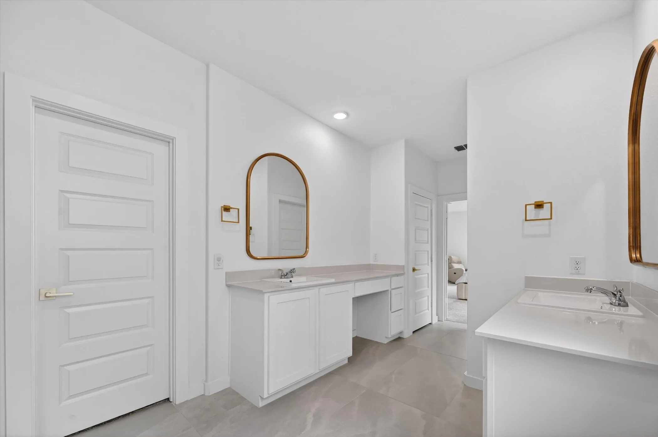 Spacious vanity area featuring dual white cabinetry, light-toned countertops, and gold-framed arched​​‌​​​​‌​​‌‌​‌‌​​​‌‌​‌​‌​‌​​​‌​​ mirrors