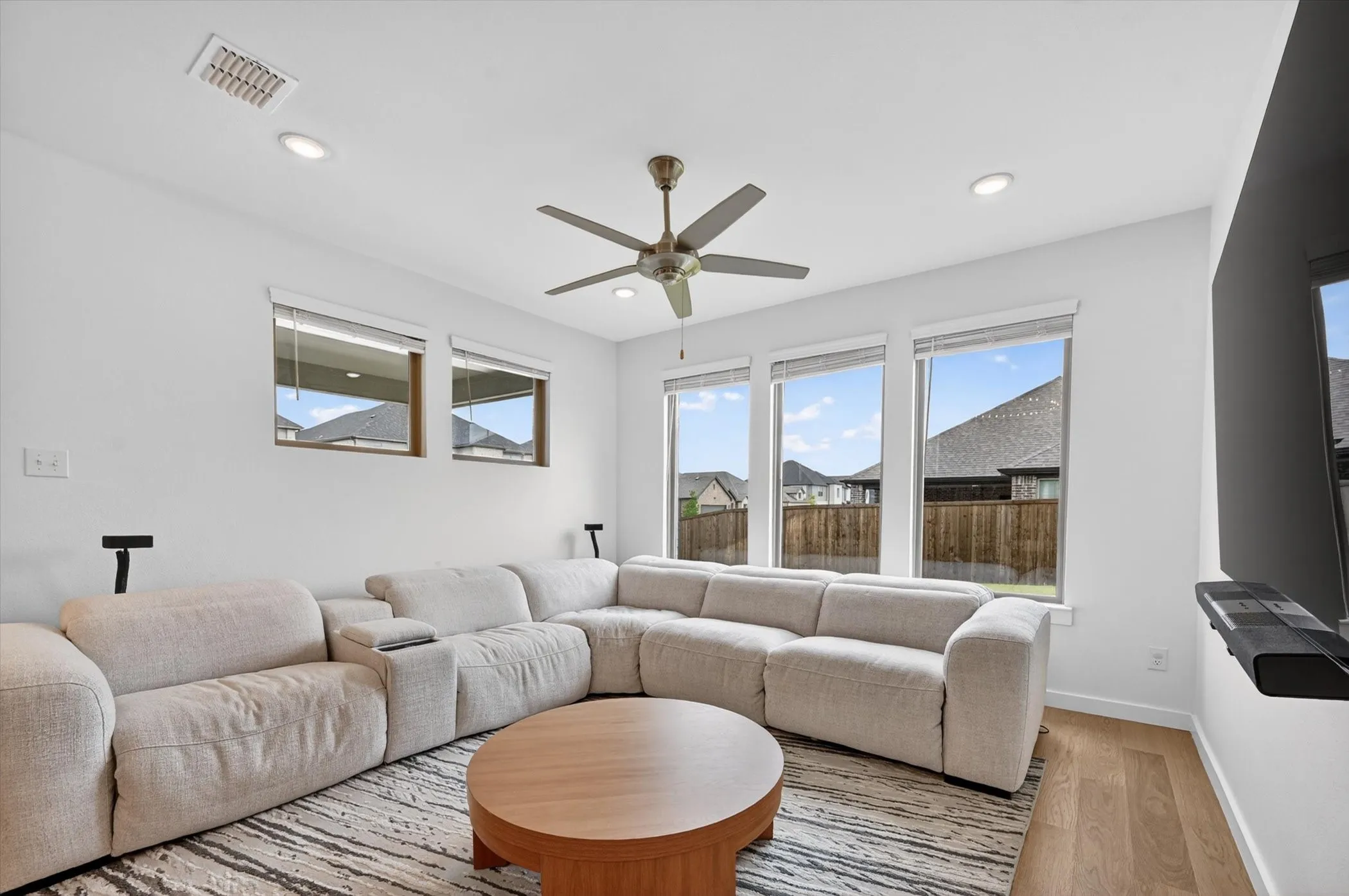 Spacious living area featuring light wood-finish flooring, a contemporary ceiling fan, recessed lighting, and multiple windows providing ample natural light