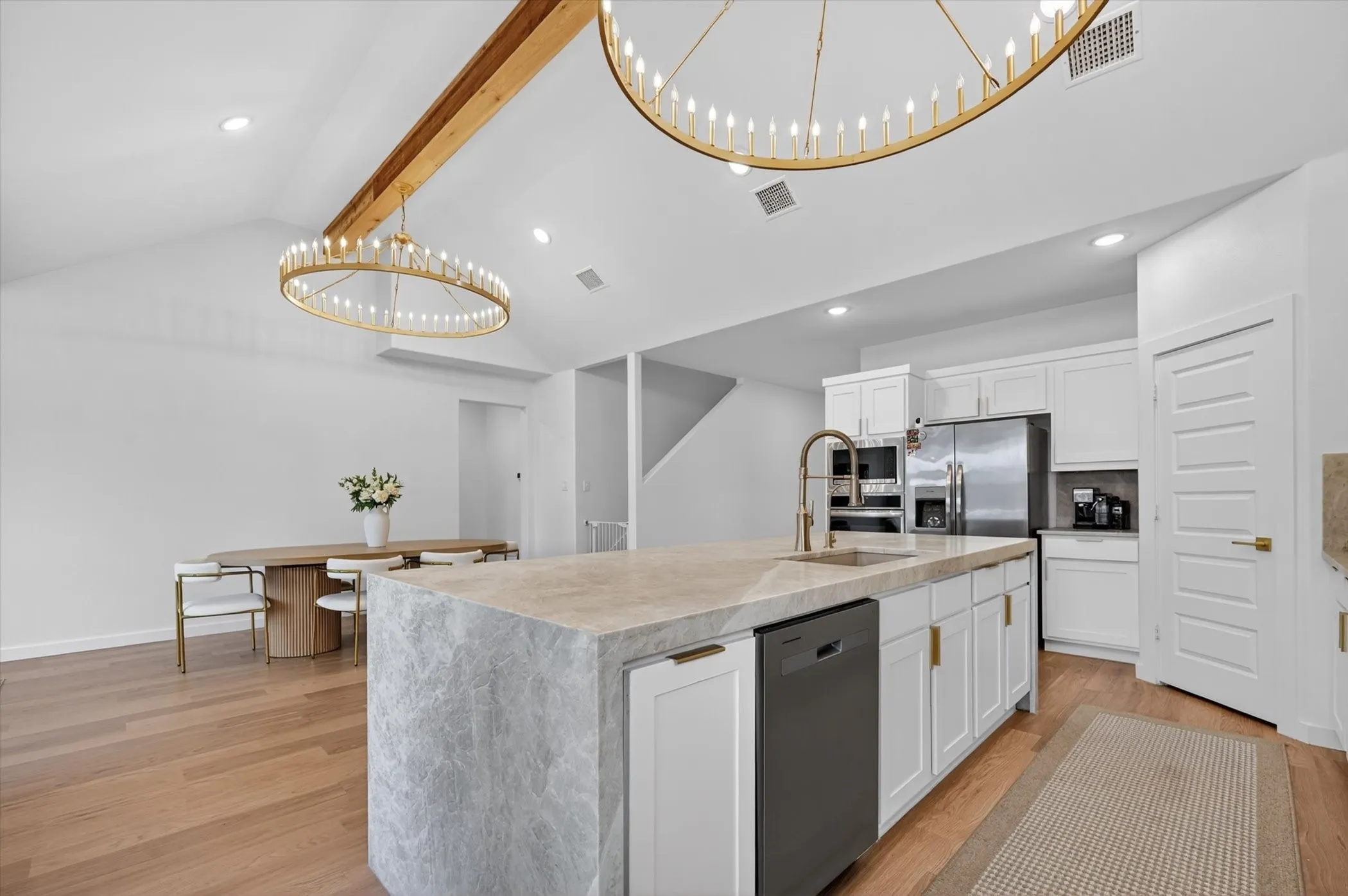 Vaulted ceiling kitchen featuring a stone-clad island, integrated sink with gooseneck faucet, stainless steel appliances, and wood-finish flooring