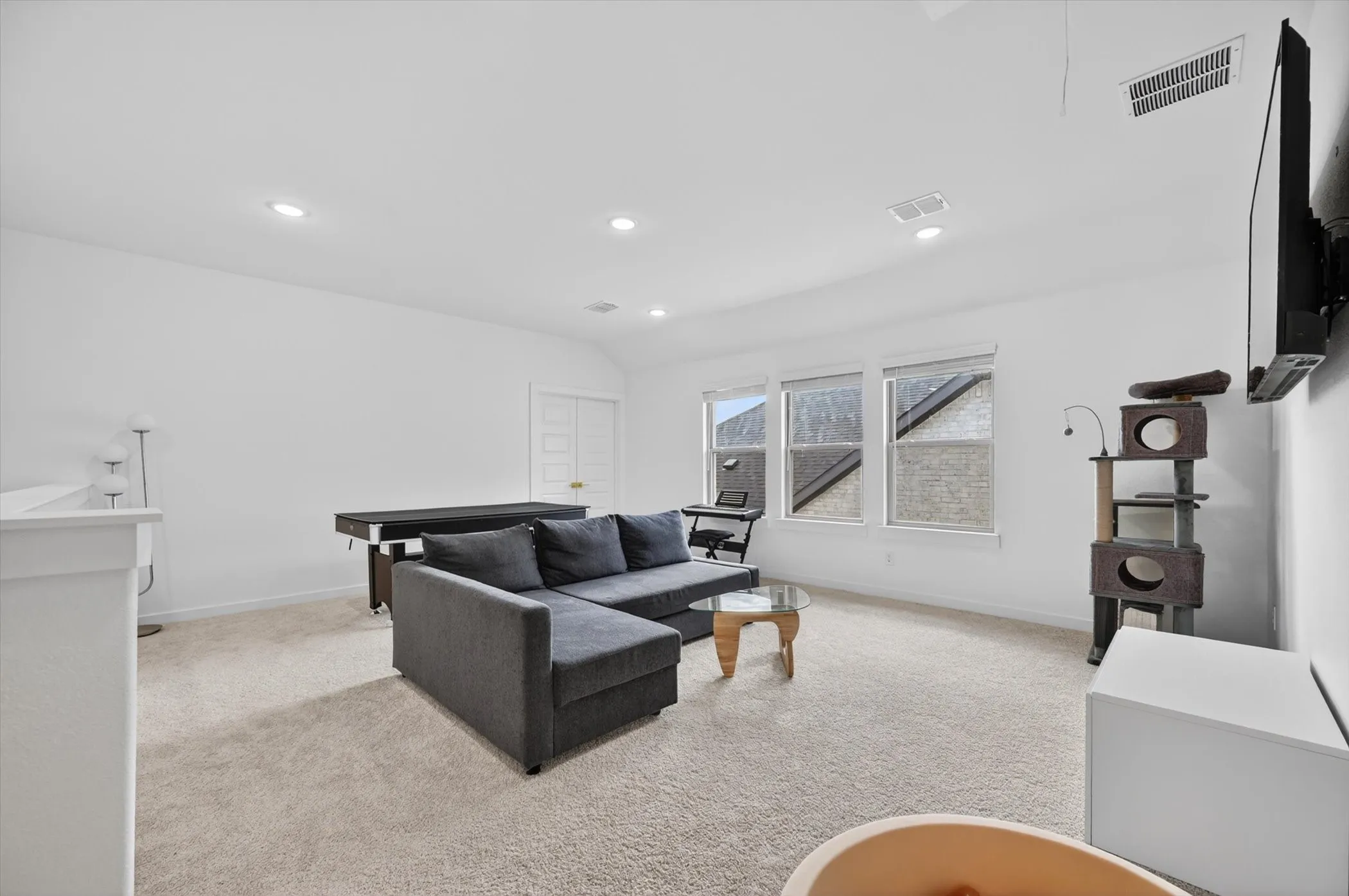 Spacious room featuring neutral carpeting, recessed lighting, white walls, and three windows providing ample natural light
