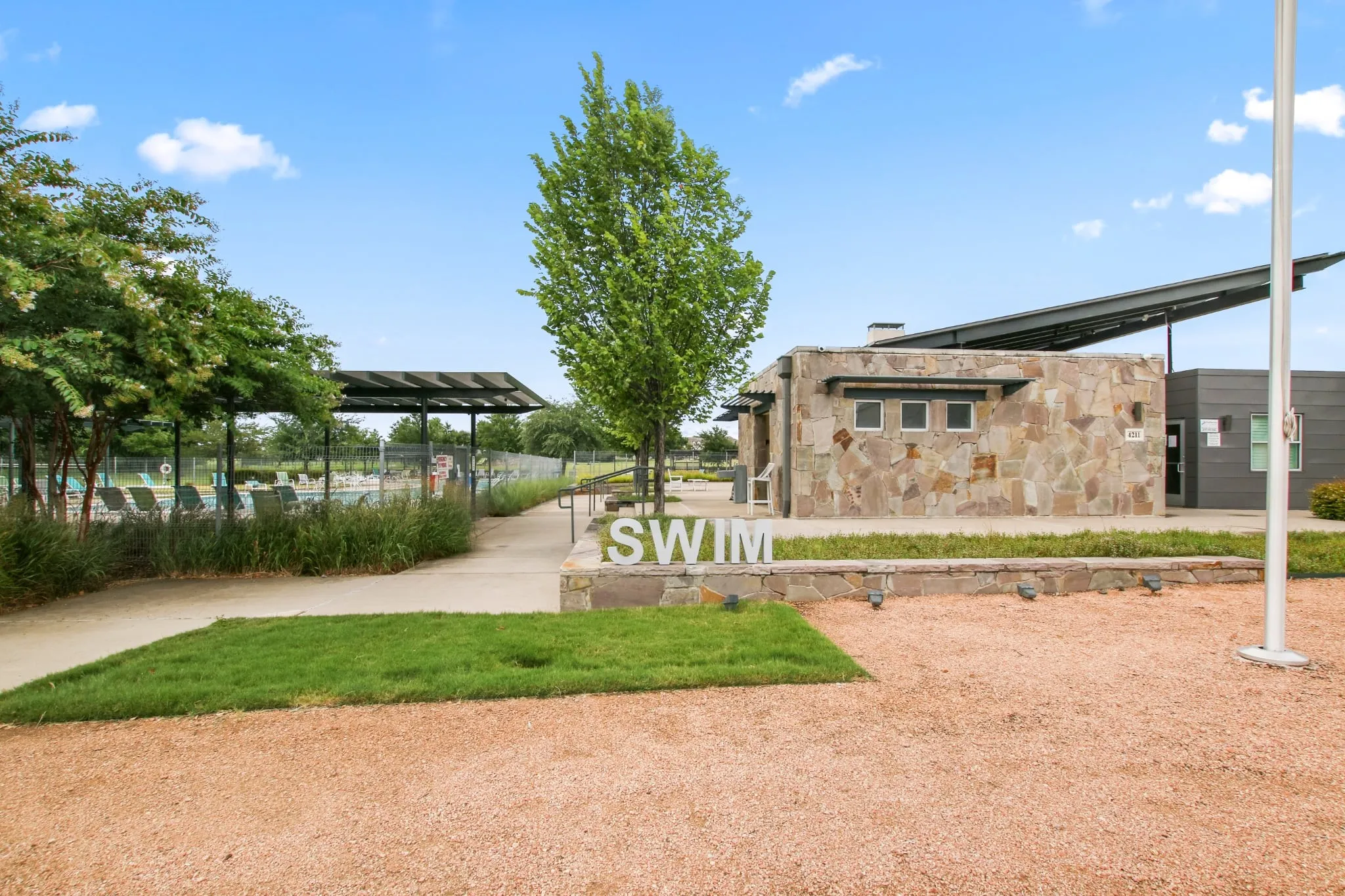 Community pool complex featuring a stone-clad building with an extended overhang, a large swimming pool, and dedicated shaded areas
