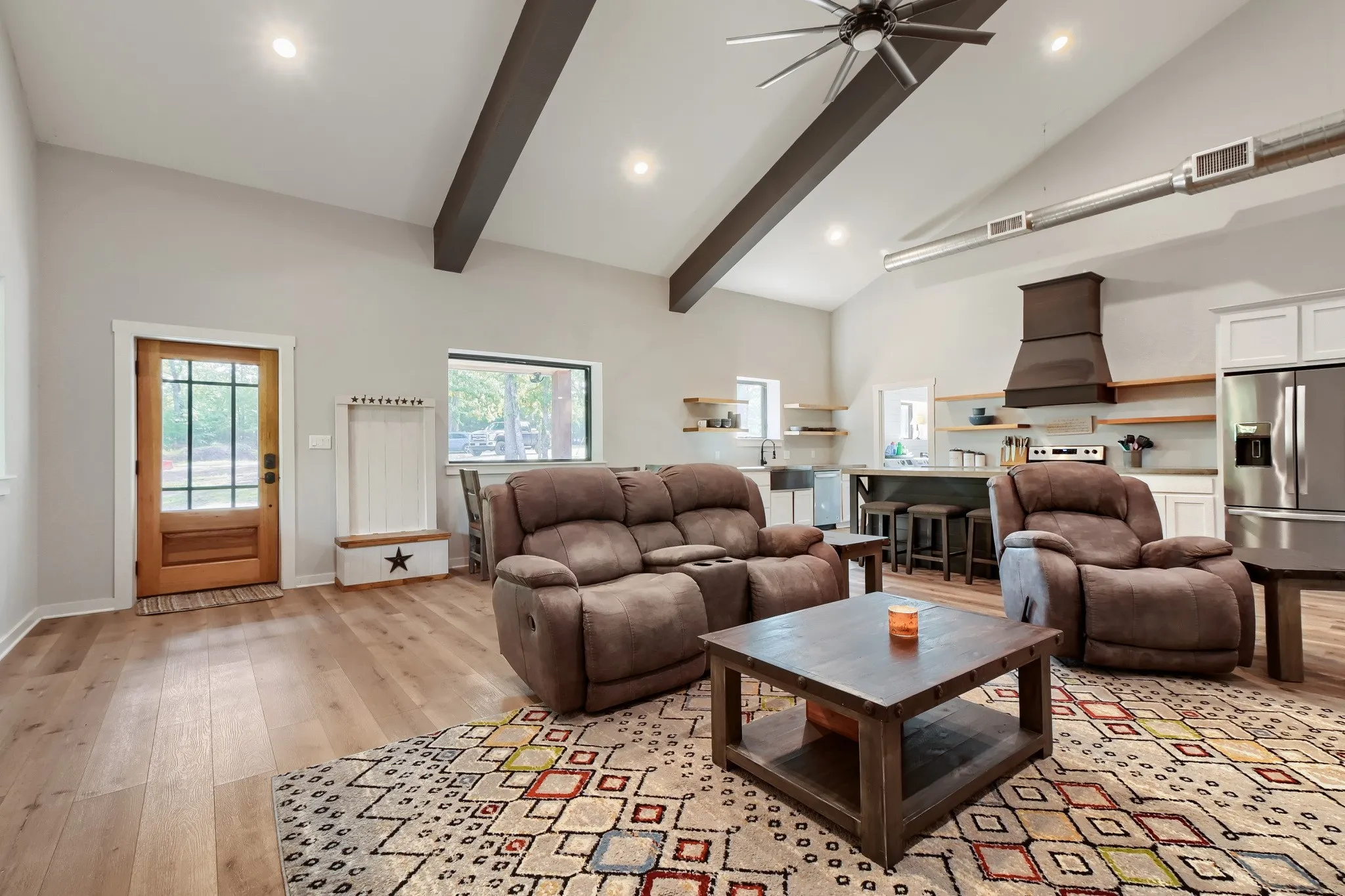 View of the open concept living area featuring vaulted ceilings with exposed beams, luxury vinyl wood flooring overlooking kitchen and dining areas.