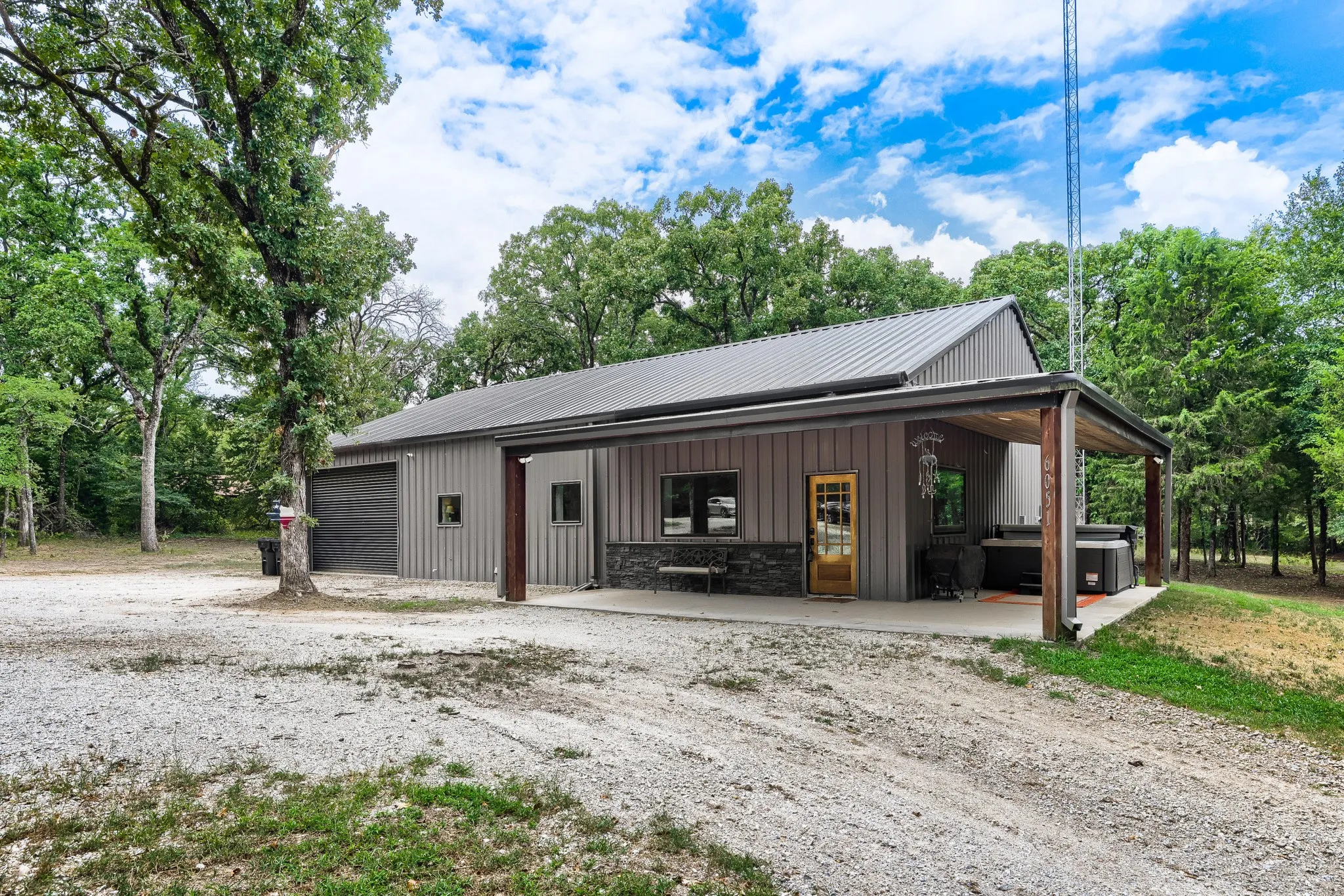 Front elevation of home featuring expansive L-shaped patio with spa, commercial overhead garage/shop door, metal siding and roof overlooking 5 private acres.