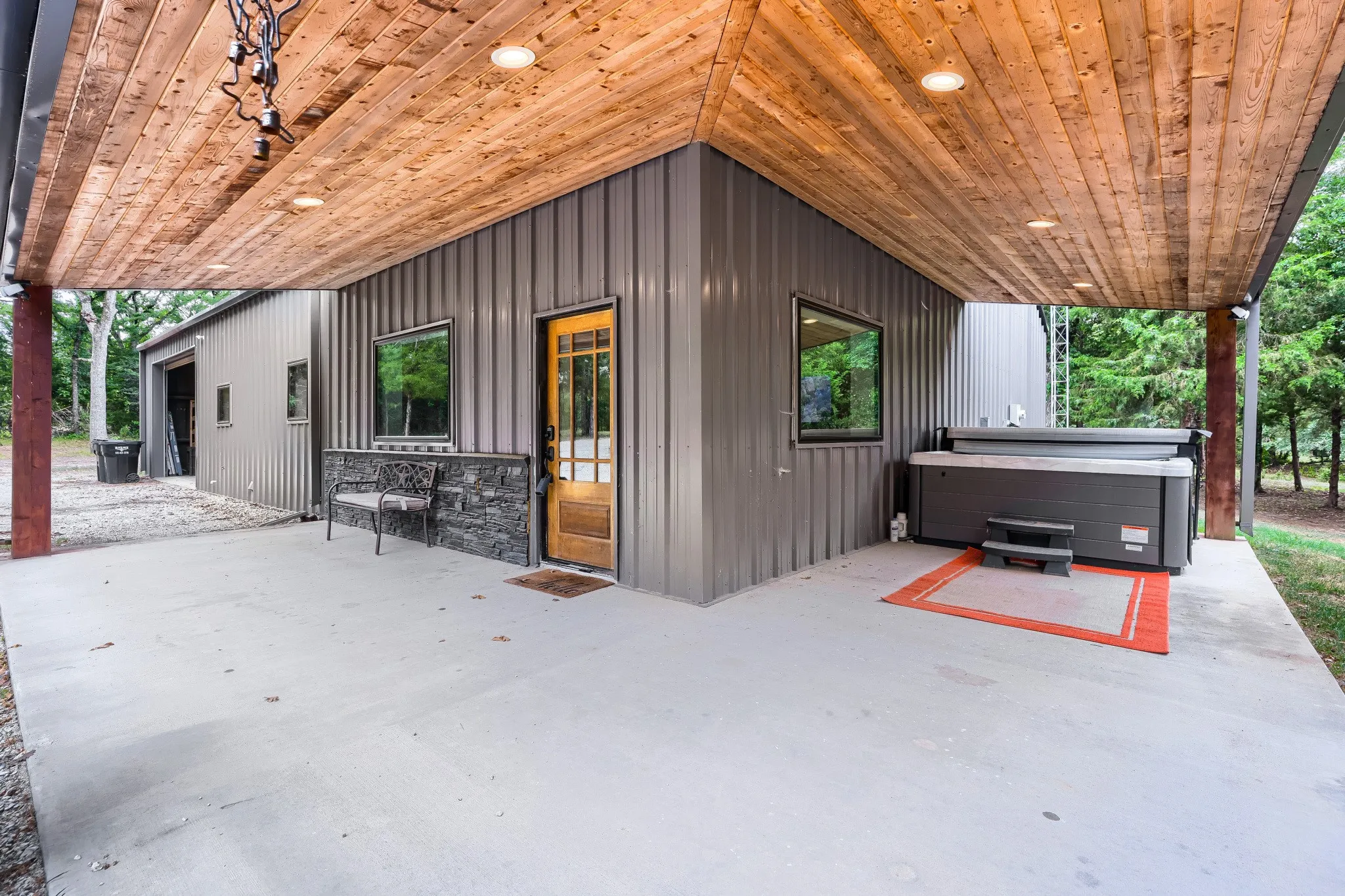 Front door entrance surrounded by expansive L-shaped patio featuring spa with a wood-plank ceiling and recessed lighting.
