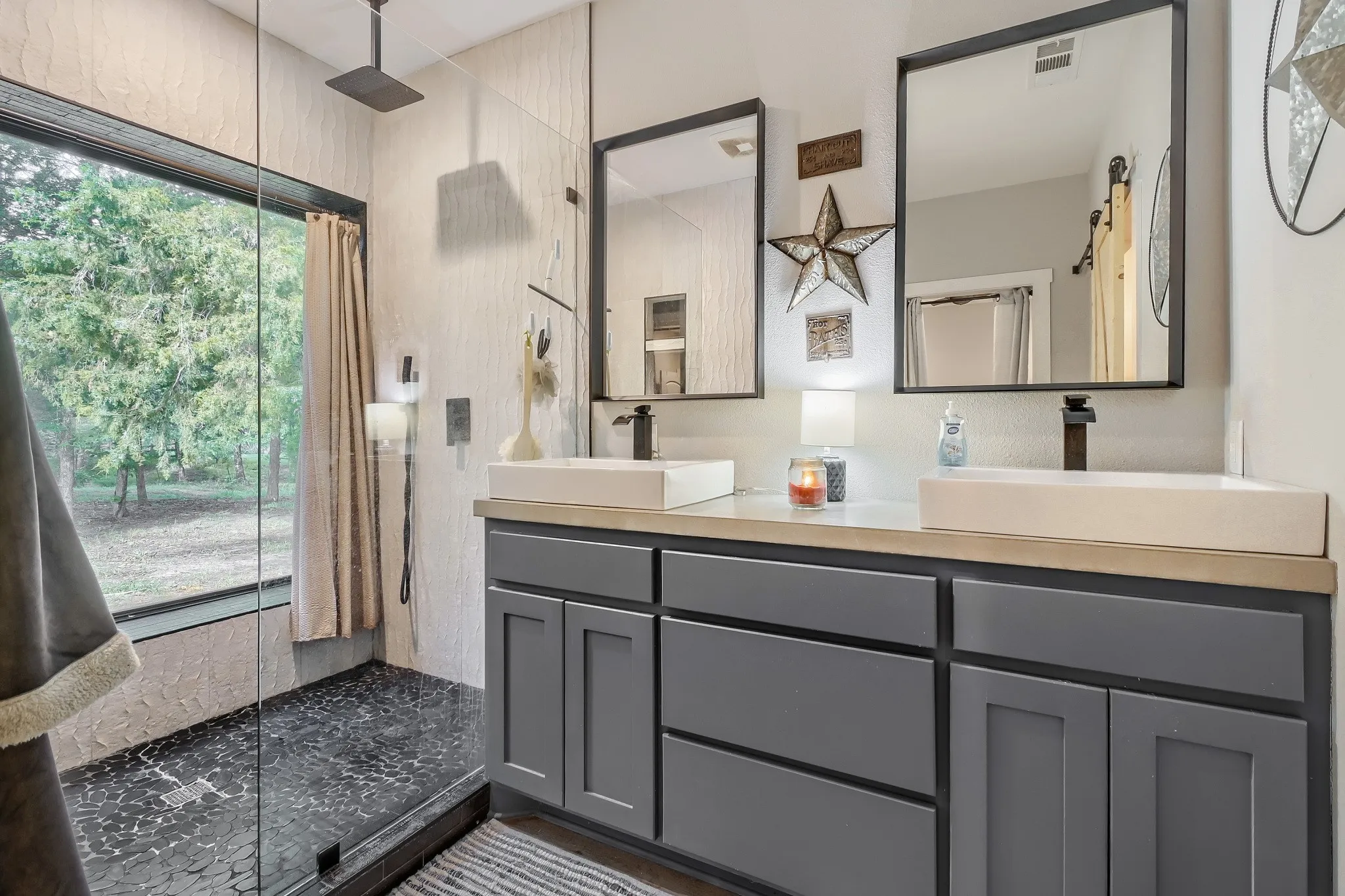 Modern farmhouse ensuite bathroom featuring a dual vanity with vessel sinks, and oversized stand-up shower with picture window overlooking 5 private acres.