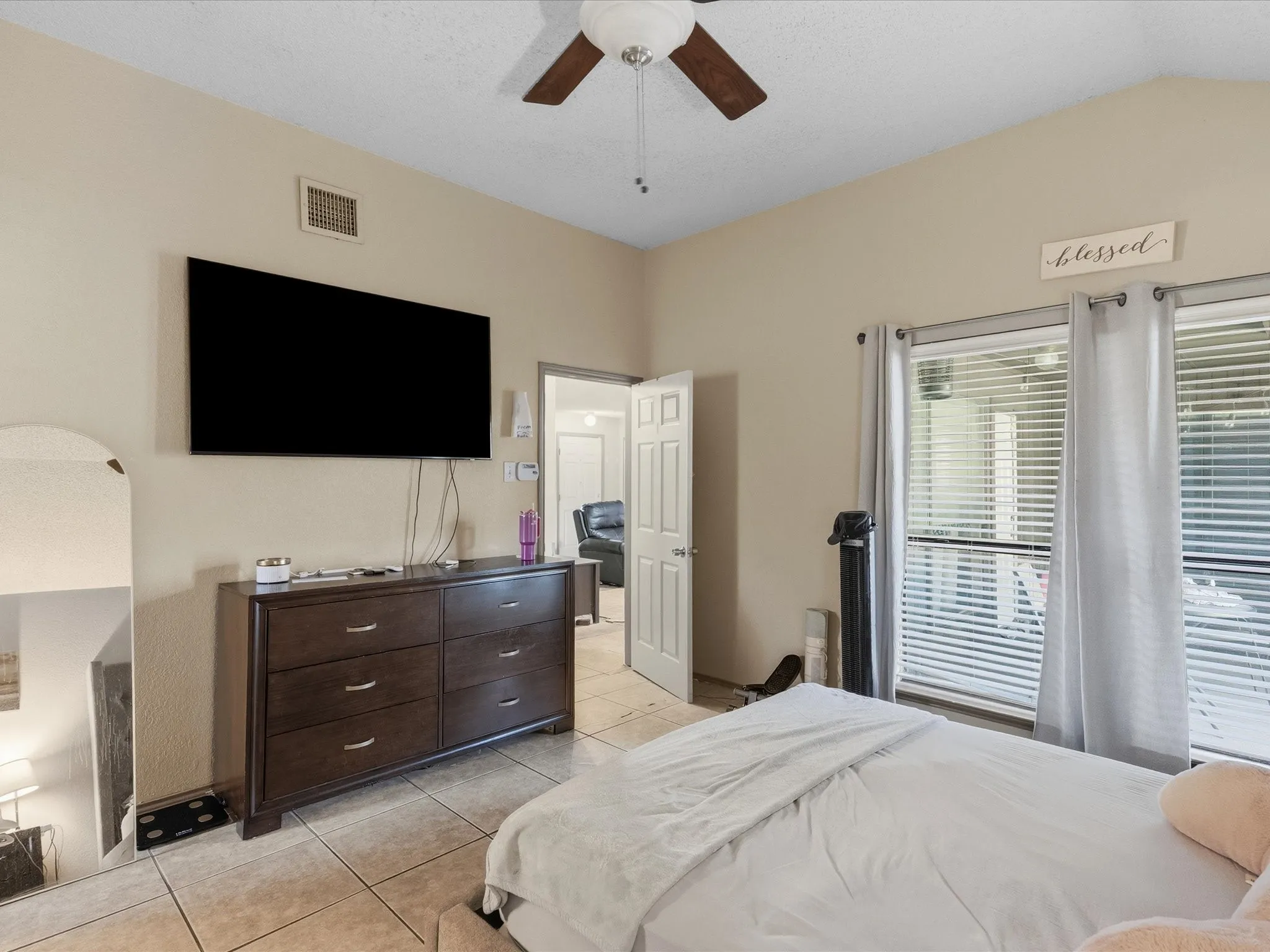 Vaulted ceiling with a ceiling fan, large window with blinds and curtain rods, tile flooring, and a doorway leading to another room