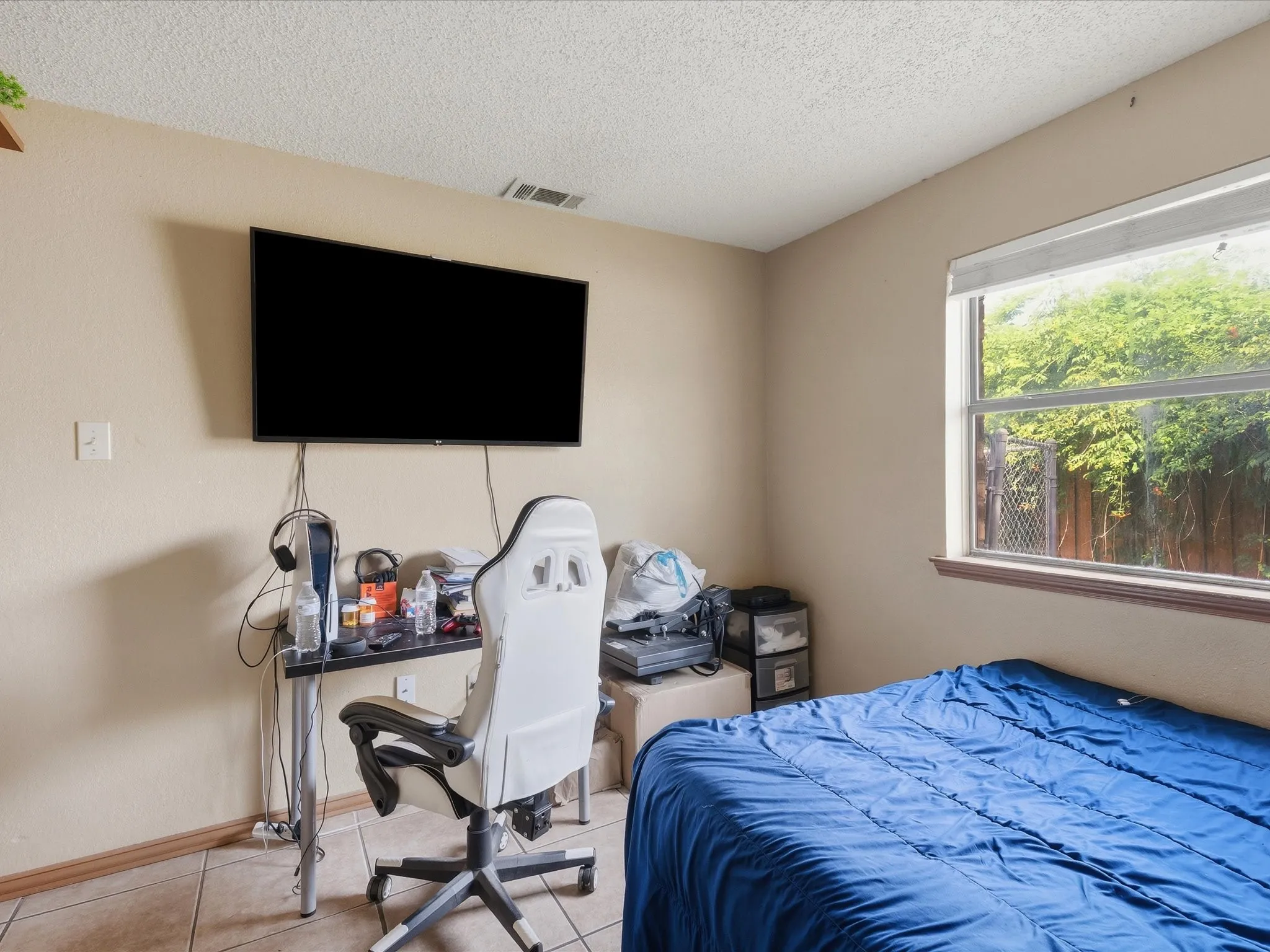 Room featuring a wall-mounted television, tiled flooring, a window with exterior foliage, and textured ceilings
