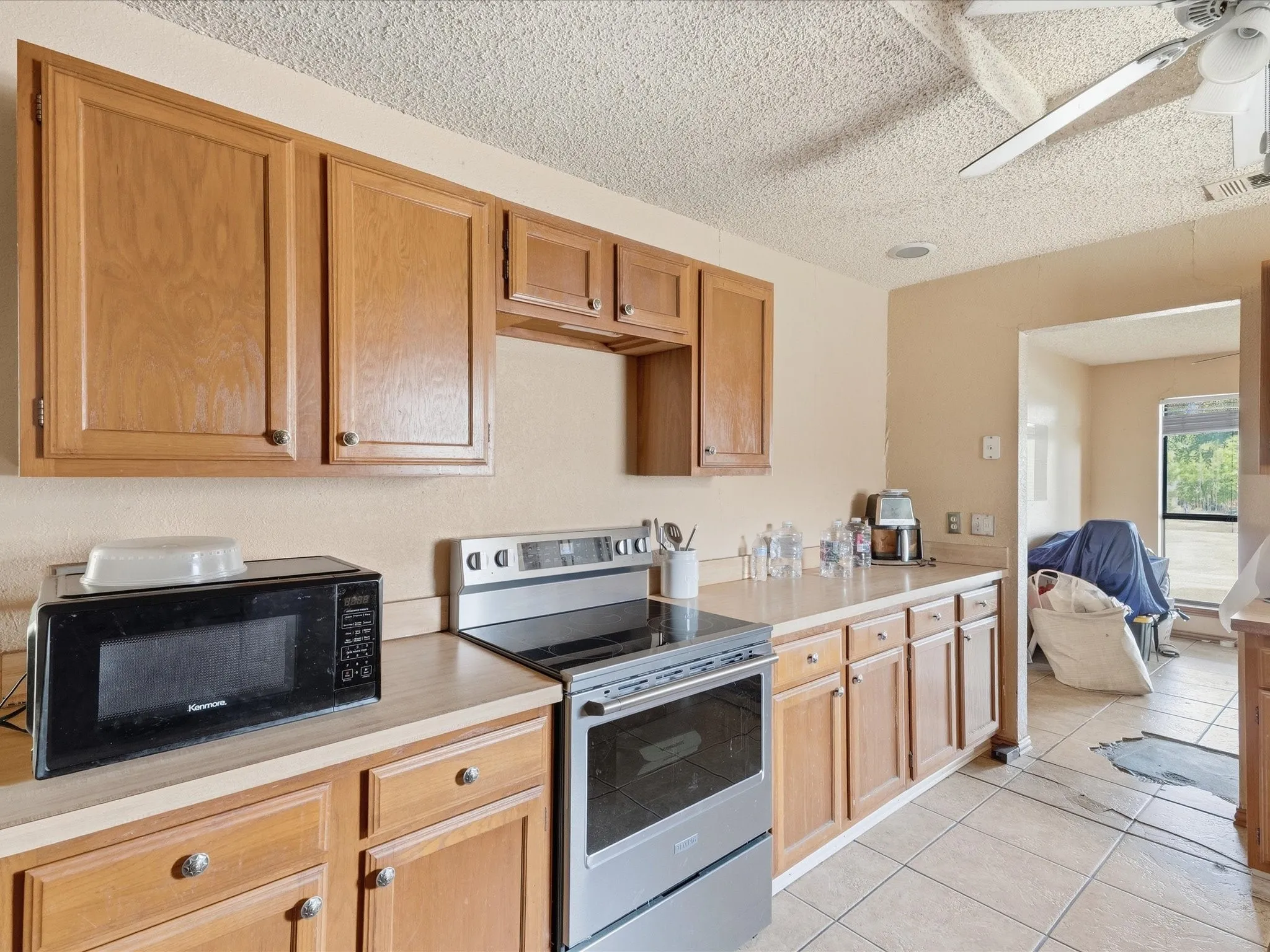 Kitchen featuring wood cabinetry, light-toned countertops, a stainless steel electric range, and ceramic tile flooring