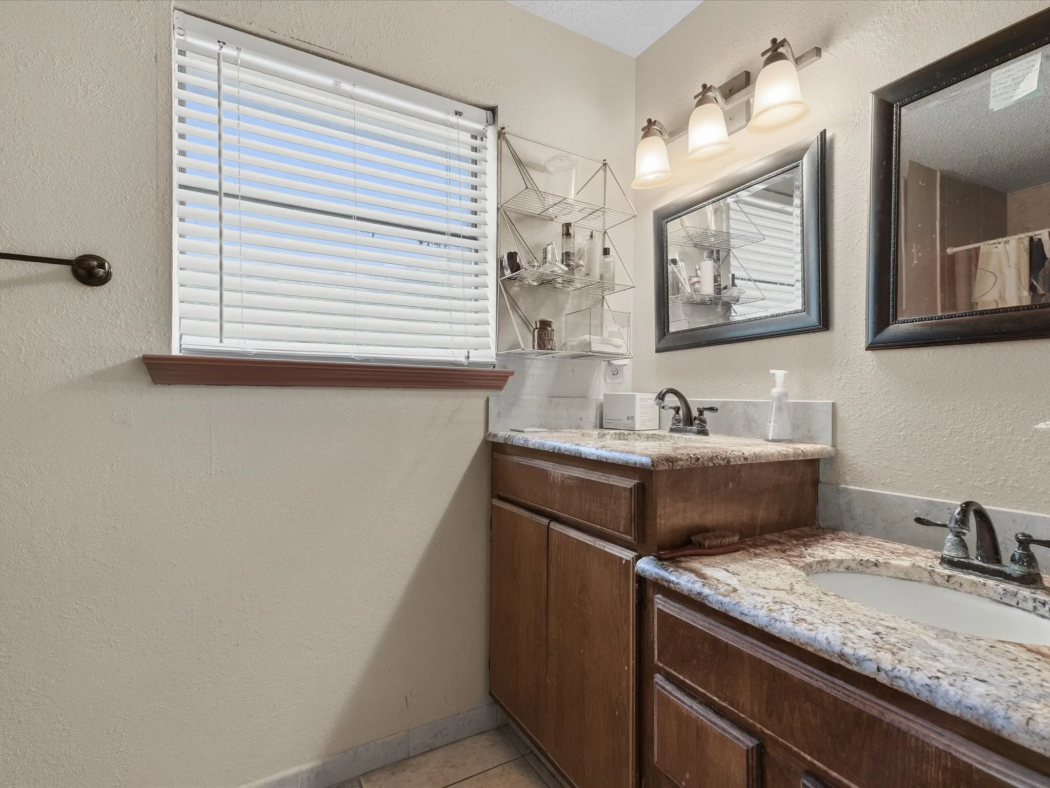 Dual vanity with granite countertops, integrated sinks, wood-finish cabinetry, and a three-light fixture above a framed mirror