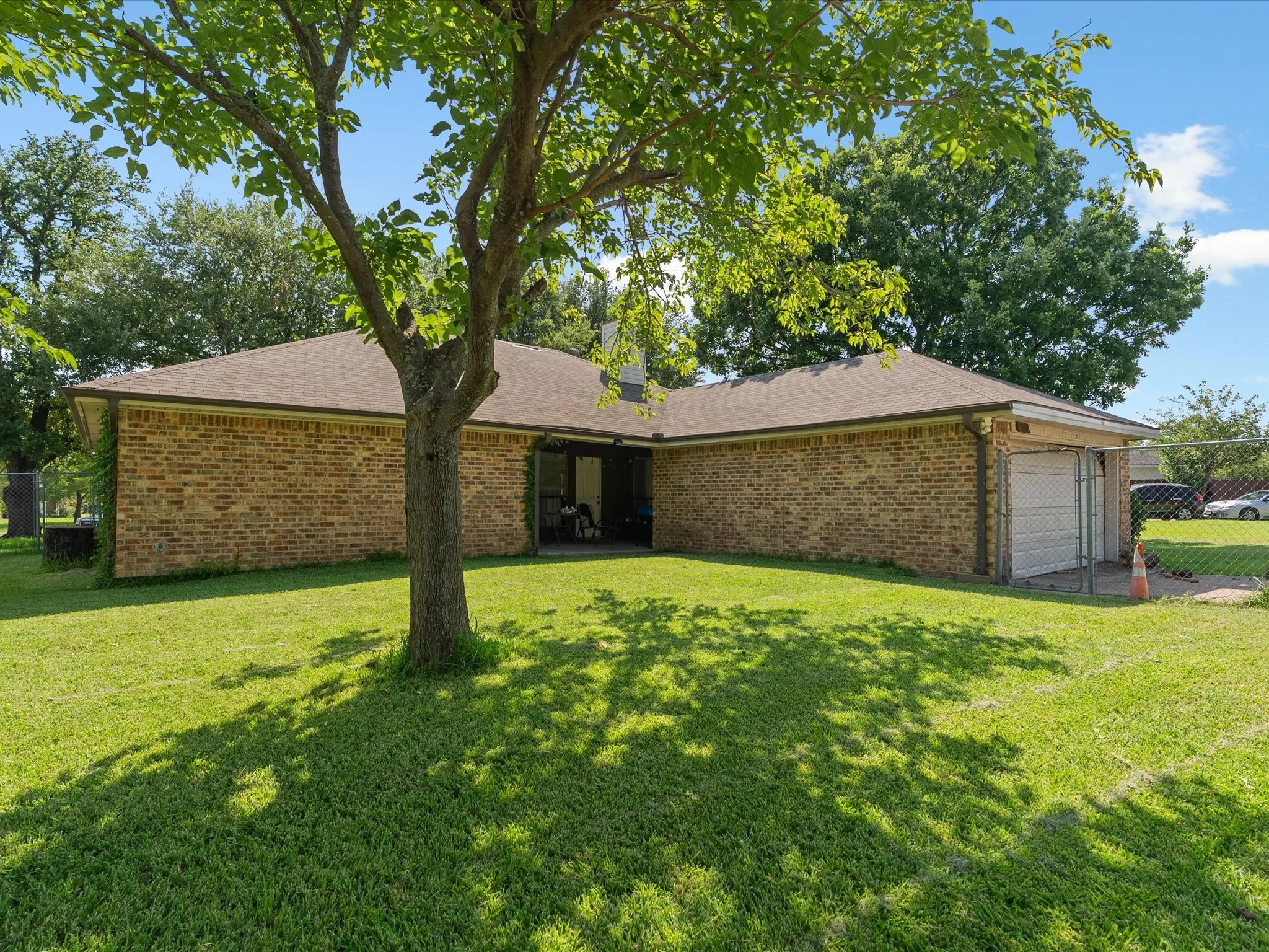 Expansive backyard featuring a mature shade tree and a brick exterior dwelling with a shingled roof