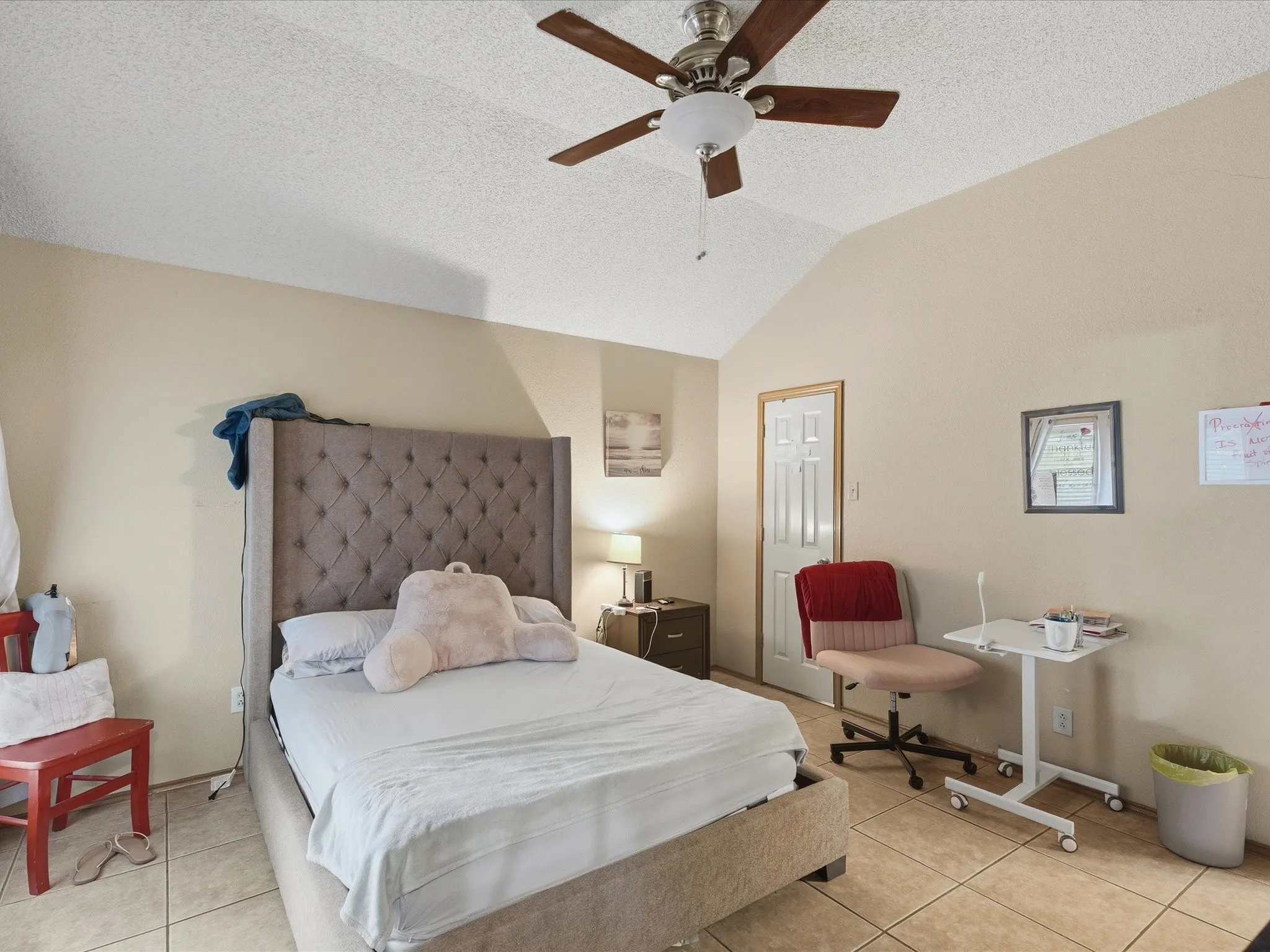 Vaulted ceiling with a ceiling fan, light tan wall color, tiled flooring, and a white paneled door
