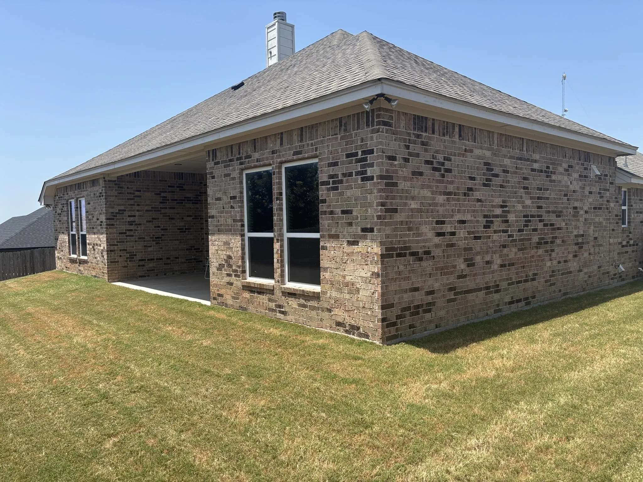 Brick exterior with a covered patio, multiple windows, and a shingled roof