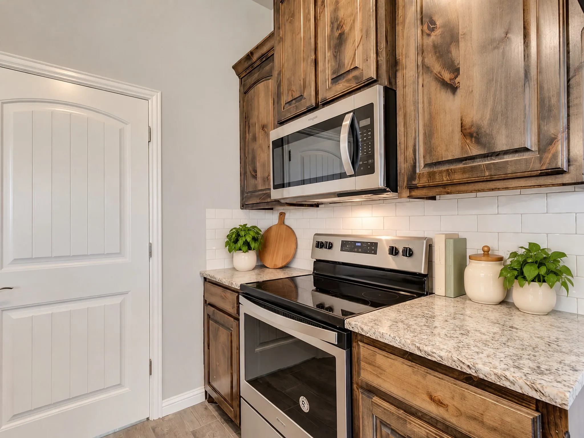 Stainless steel appliances, wood-finish cabinetry, subway tile backsplash, light-toned countertops, and a white paneled door