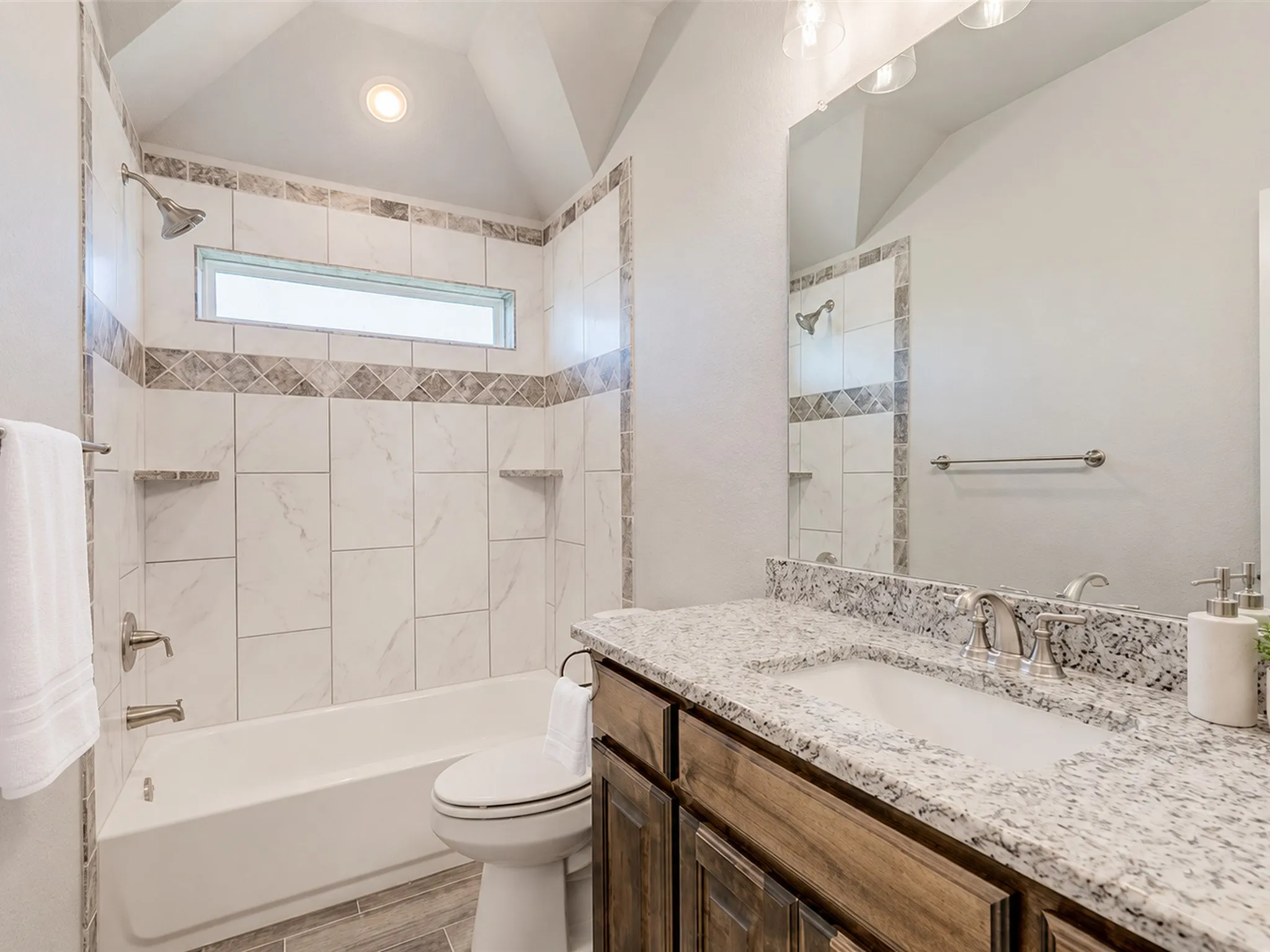 Bathroom featuring a white tub, tiled shower surround with a mosaic accent, a vanity with a white countertop and built-in sink, and wood-finish cabinetry