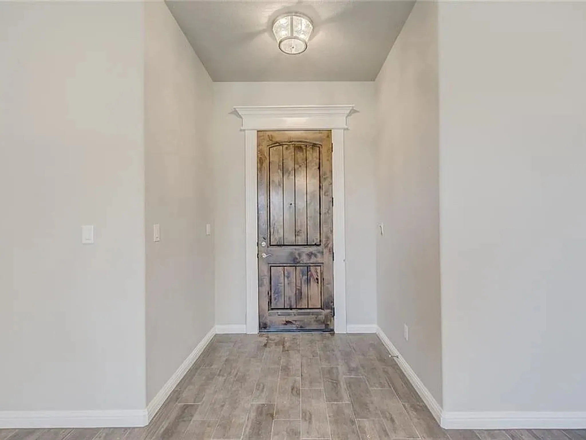 Foyer featuring wood-look tile flooring, light neutral wall tones, decorative ceiling light fixture, and a solid wood entry door with ornate trim